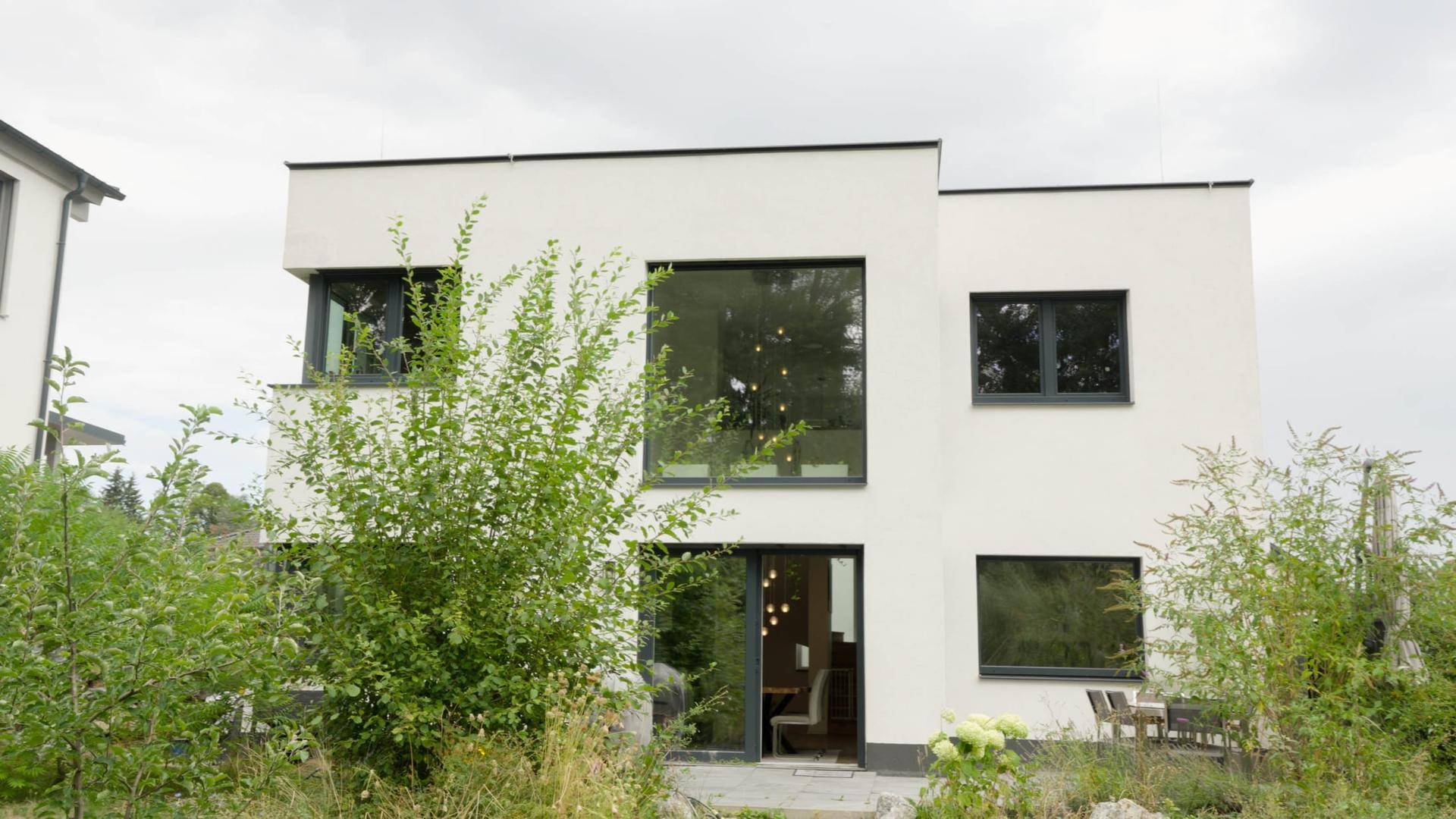Modernes Einfamilienhaus mit weißer Fassade und großen Fenstern im Grünen.