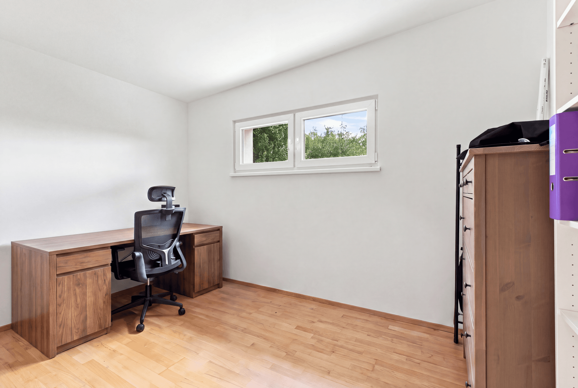 Helles Arbeitszimmer mit Holzboden, Schreibtisch und Fenster mit Blick ins Grüne.