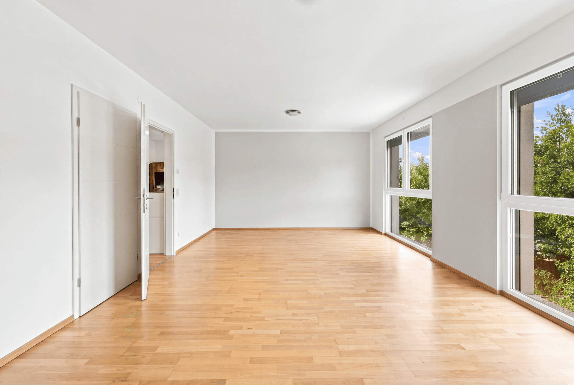 Geräumiges, leeres Zimmer mit Holzboden und großen Fenstern, ideal für individuelle Gestaltung.