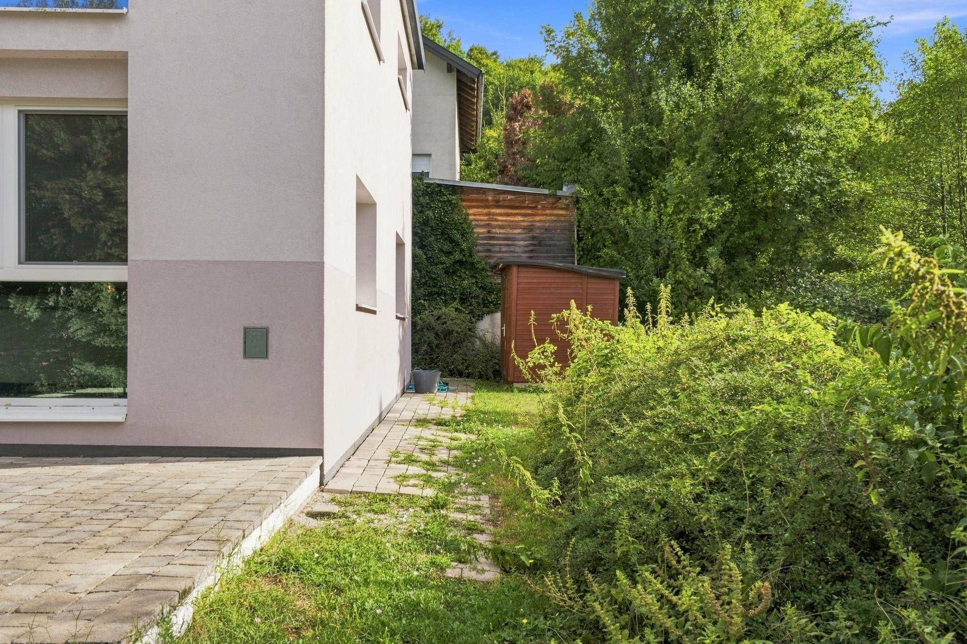 Seitlicher Gartenbereich des Hauses mit Rasenfläche, Sträuchern und einem kleinen Schuppen.