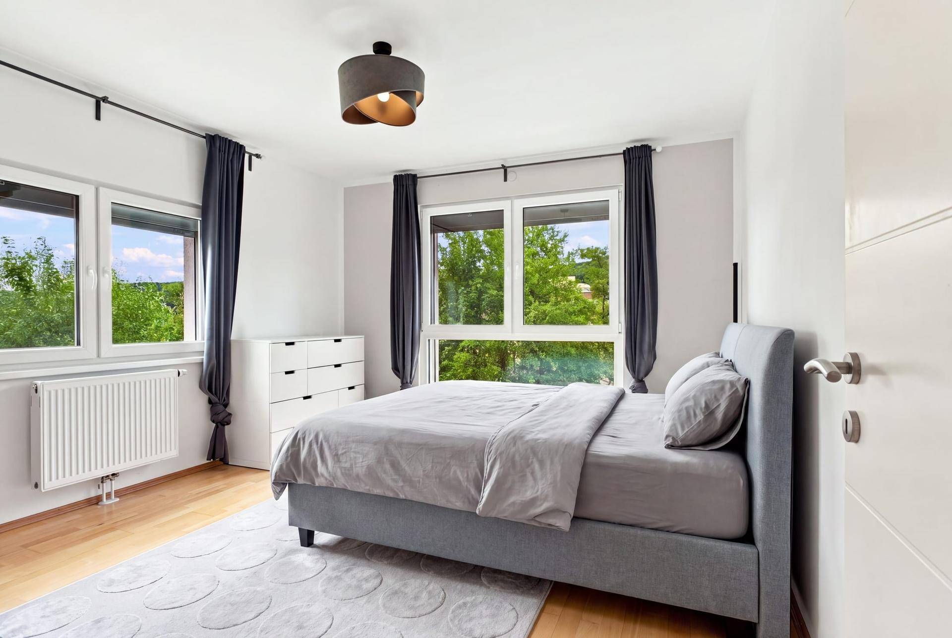 Schlafzimmer mit Doppelbett, Teppich und großen Fenstern mit Blick ins Grüne.