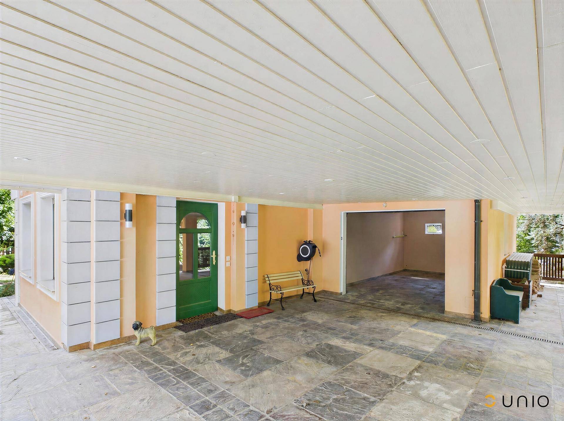 Überdachter Eingangsbereich mit Carport und Zugang zur Garage, gepflasterter Boden.