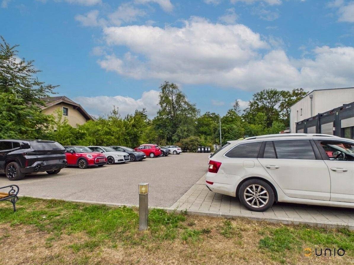 Großer Parkplatz mit mehreren Fahrzeugen neben dem Ärztezentrum, umgeben von Grün.