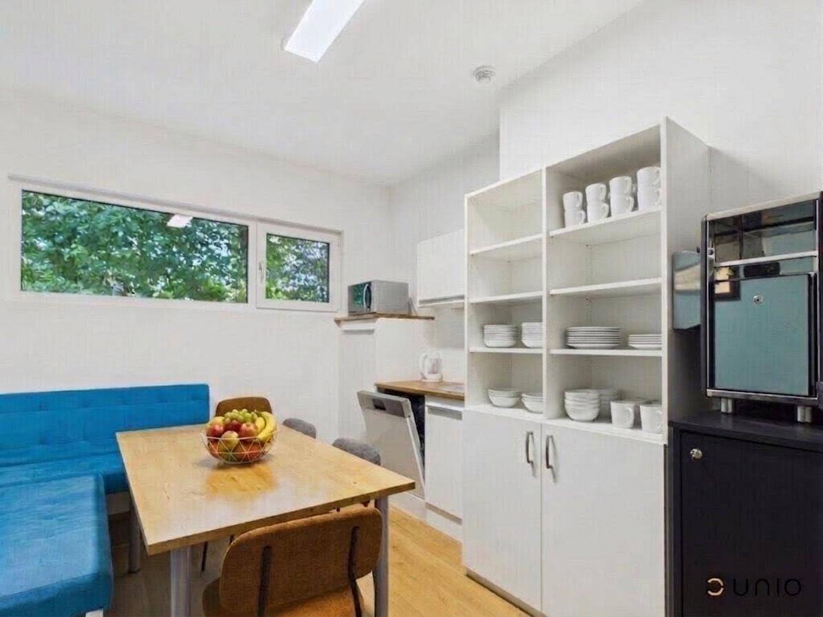Funktionale Teeküche mit Essbereich, weißen Schränken und Fenster mit Grünblick.