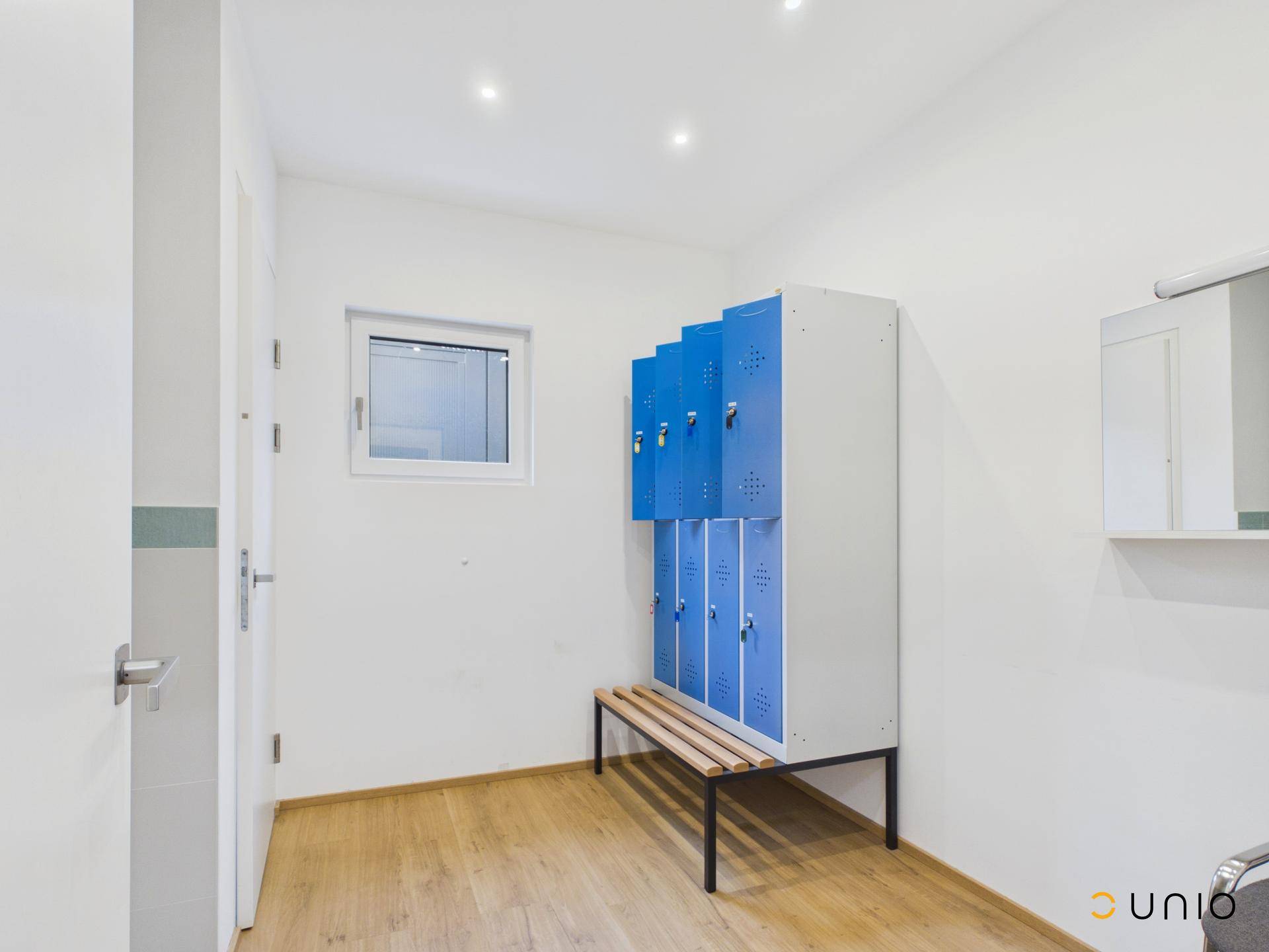 Kleiner Raum mit blauen Spinden, Sitzbank und Fenster, ideal als Umkleidebereich.