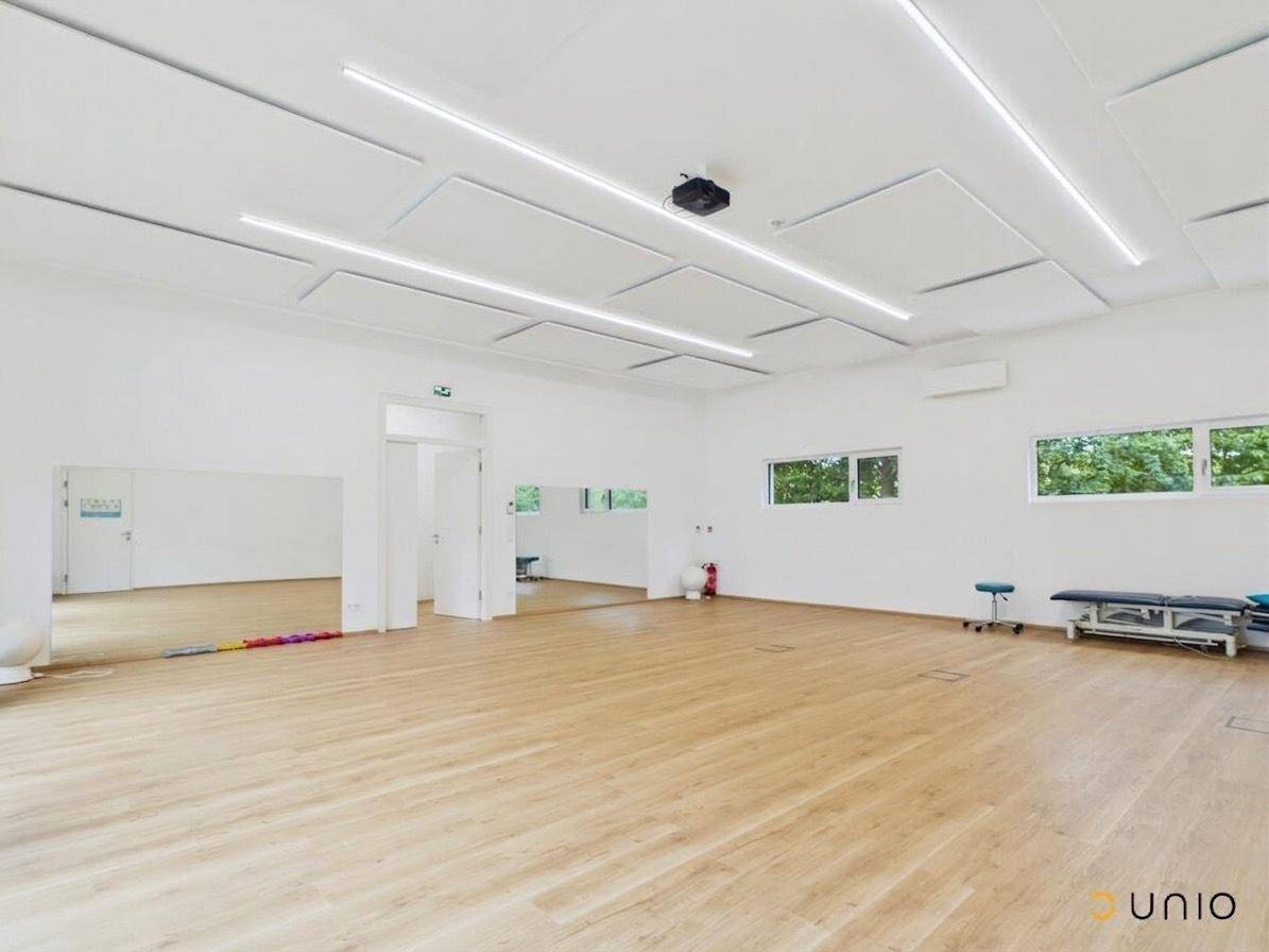 Geräumiger, heller Raum mit Holzfußboden, Spiegelwand und moderner Deckenbeleuchtung.