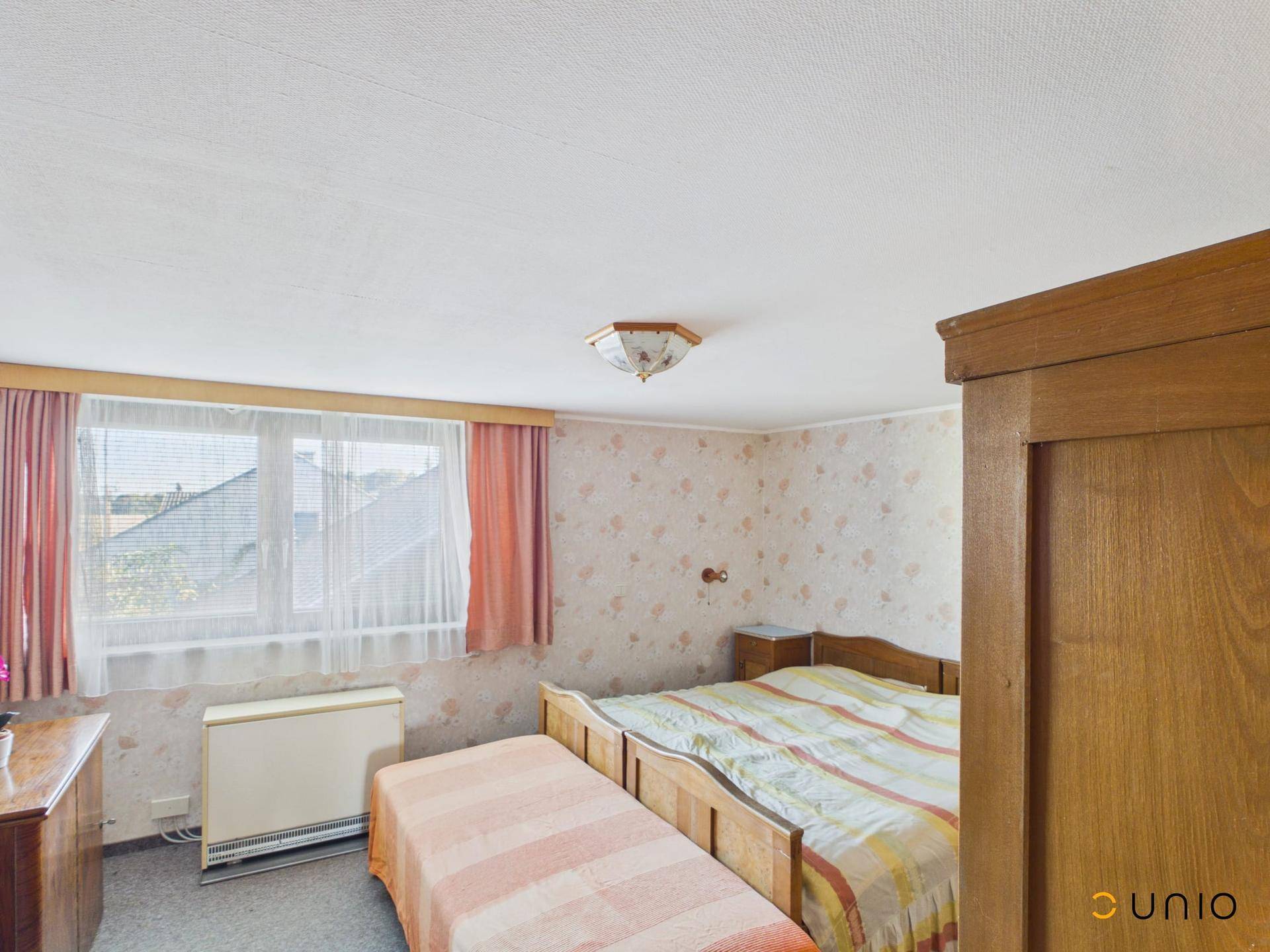 Schlafzimmer mit floraler Tapete, zwei Betten und Fenster mit Blick auf die Nachbarschaft.