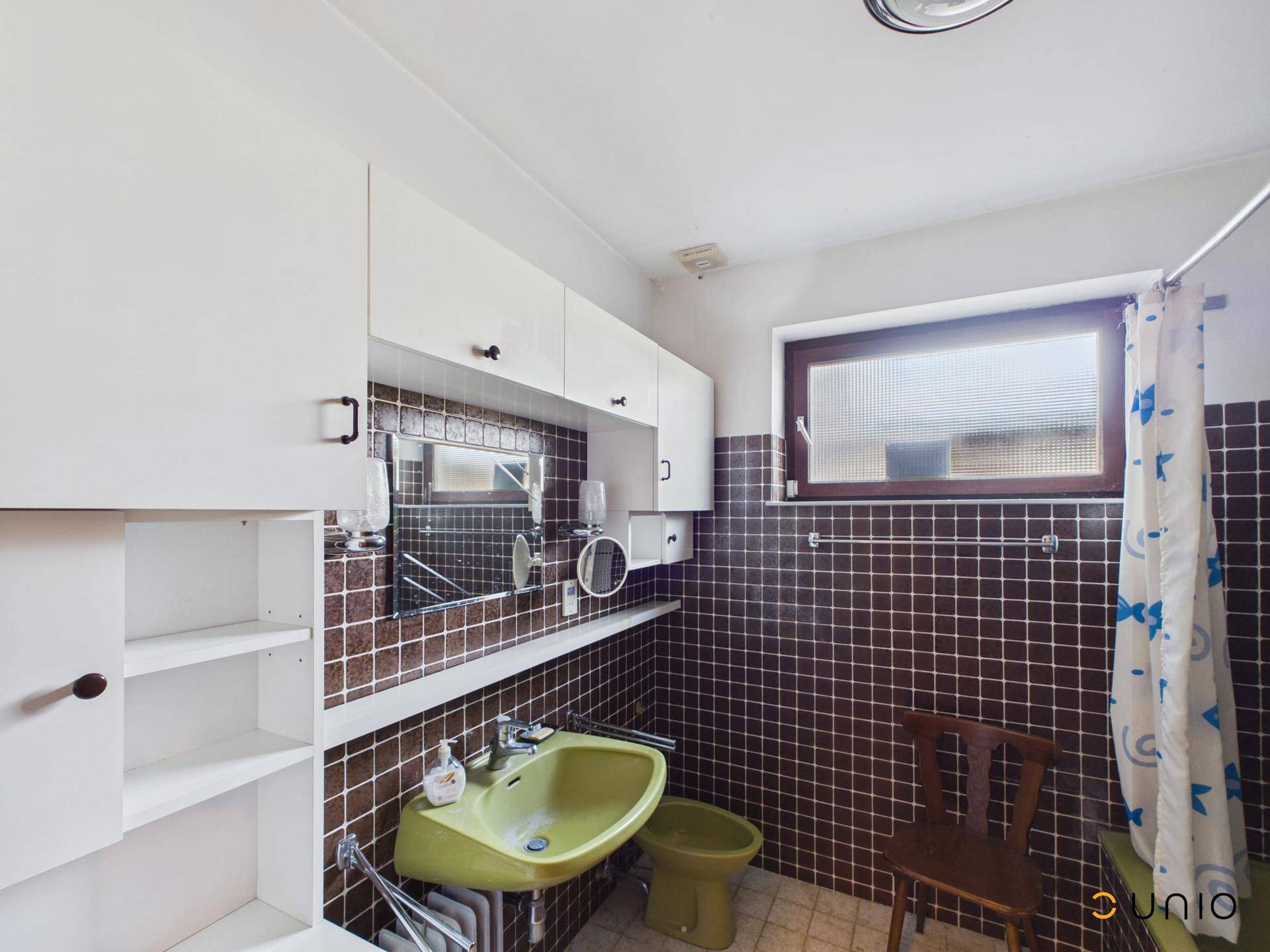 Badezimmer im Stil der 80er Jahre mit braunen Fliesen, grünem Waschbecken und Fenster.