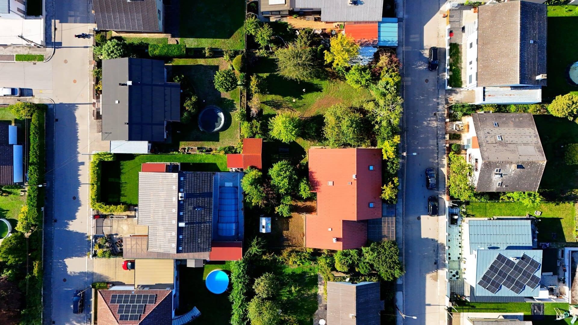 Luftaufnahme einer Wohnsiedlung mit grünen Gärten, Häusern und angrenzenden Straßen.