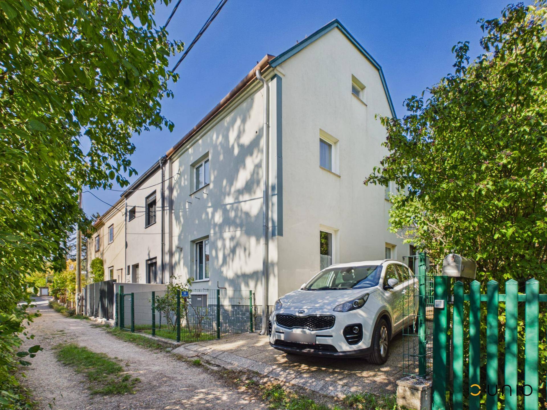 Seitenansicht des Hauses mit gepflegter Fassade, Vorgarten und geparktem Auto auf dem Stellplatz.