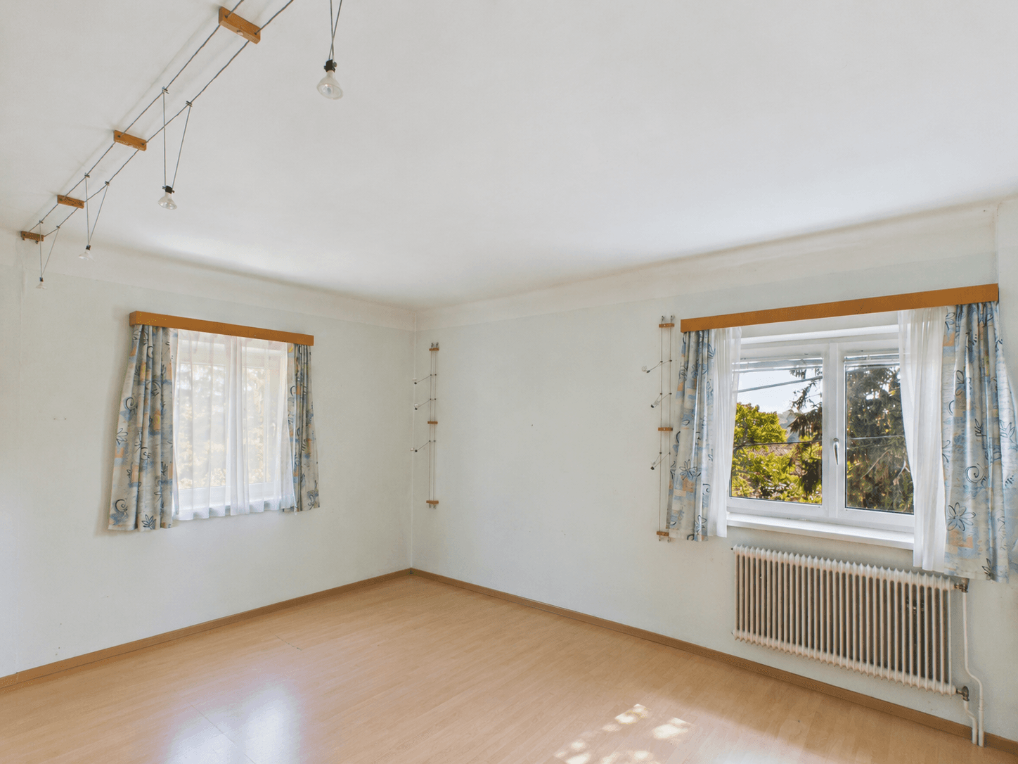 Helles Schlafzimmer mit Laminatboden, zwei Fenstern und einem angenehmen Blick ins Grüne.