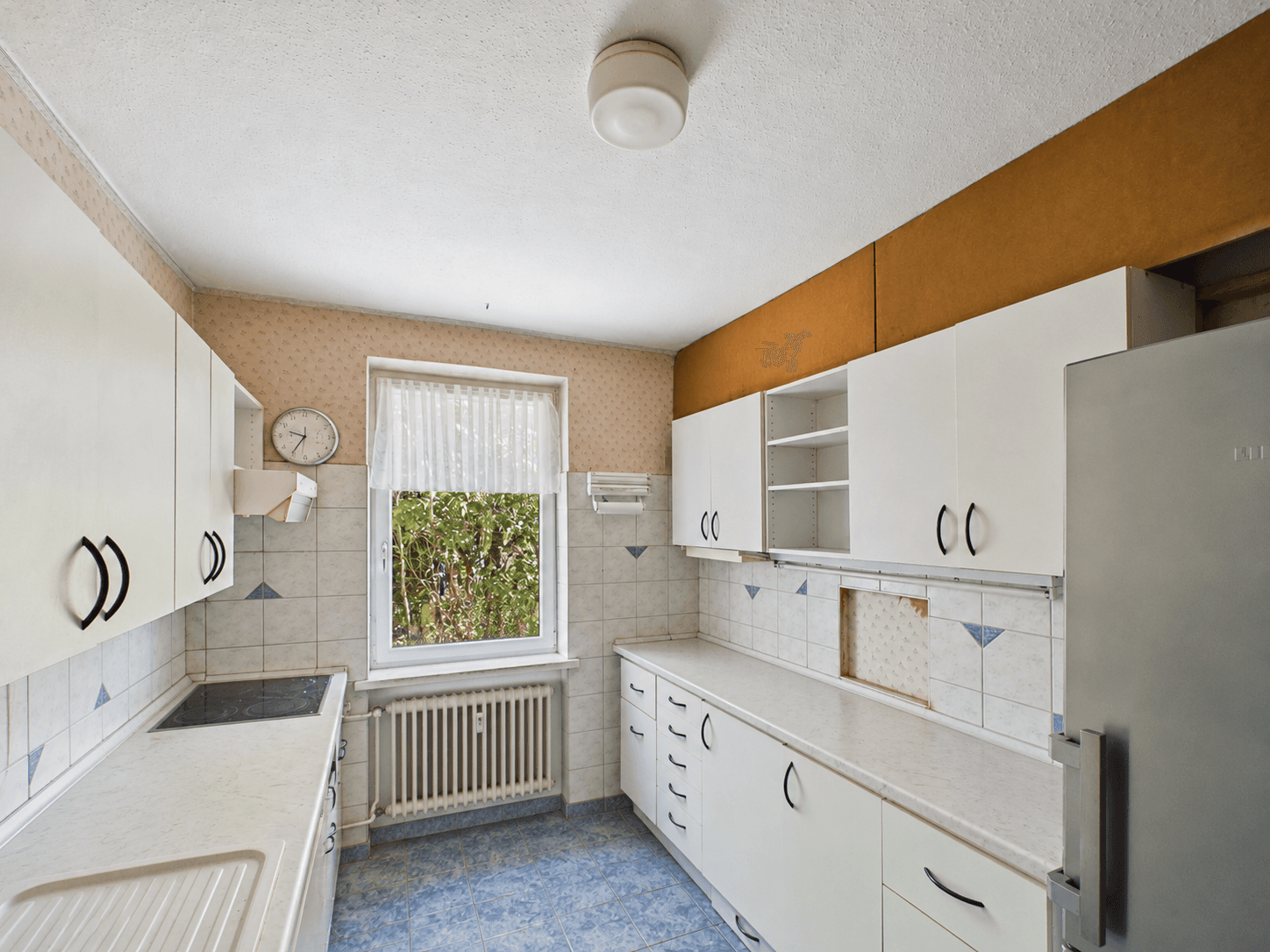 Funktionale Küche mit weißen Schränken, blauen Fliesen und Fenster zum Gartenbereich.