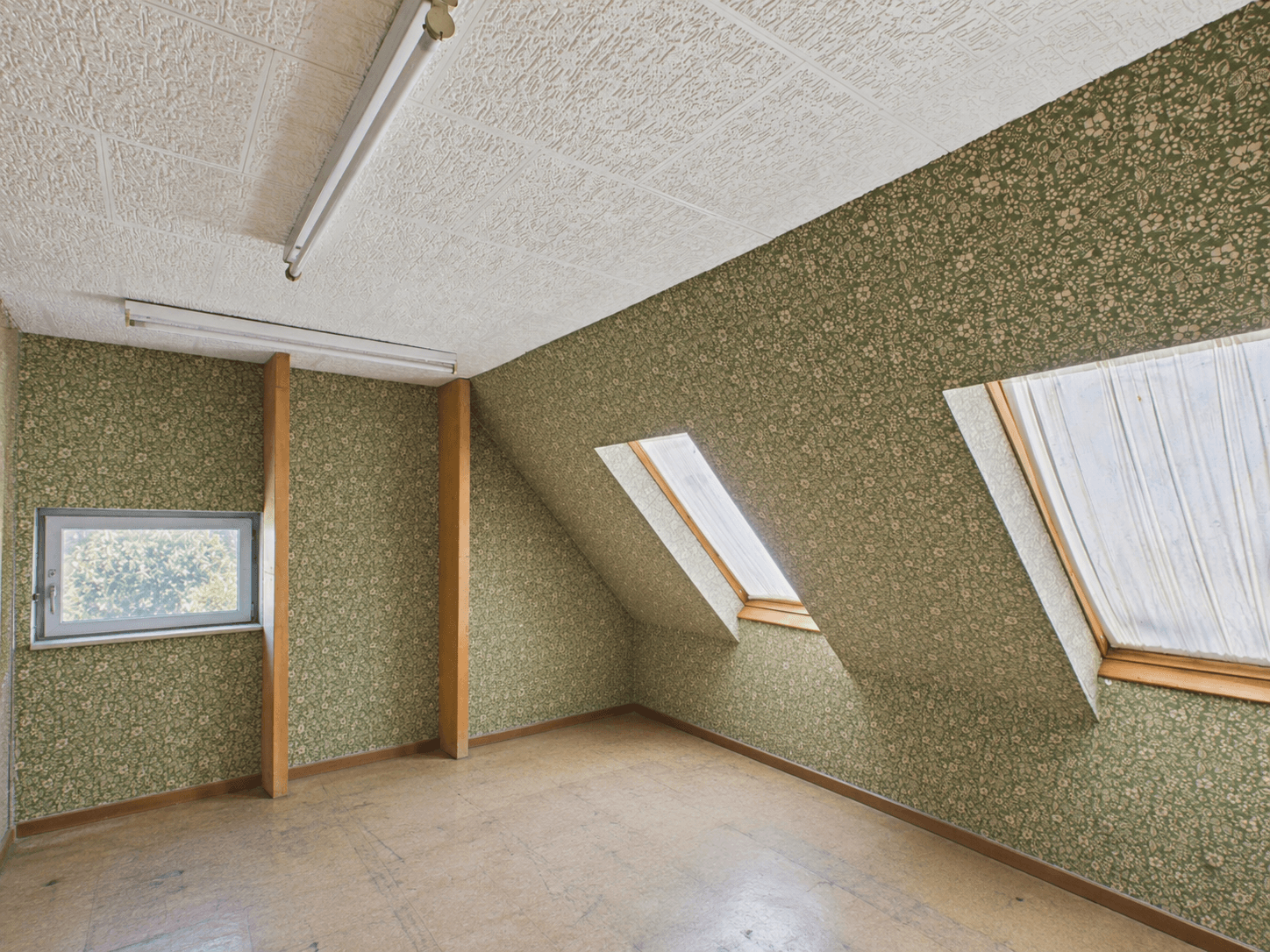 Dachzimmer mit Schrägen, Dachfenstern und gemusterter Tapete, ideal zum Ausbau.