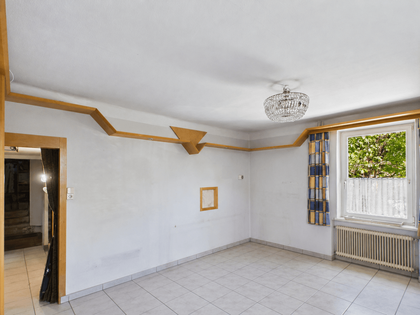 Helles Wohnzimmer mit Fliesenboden, schlichten Wänden und einem Fenster mit Blick nach draußen.
