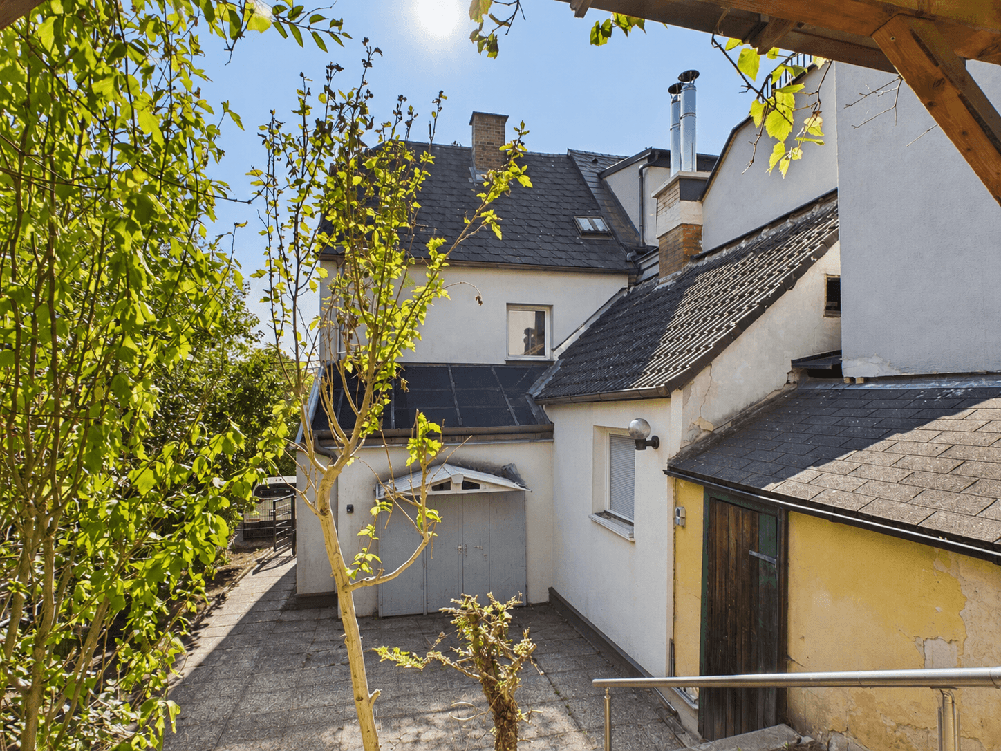 Rückansicht des Hauses mit Nebengebäuden, gepflastertem Hof und viel Grün im Gartenbereich.