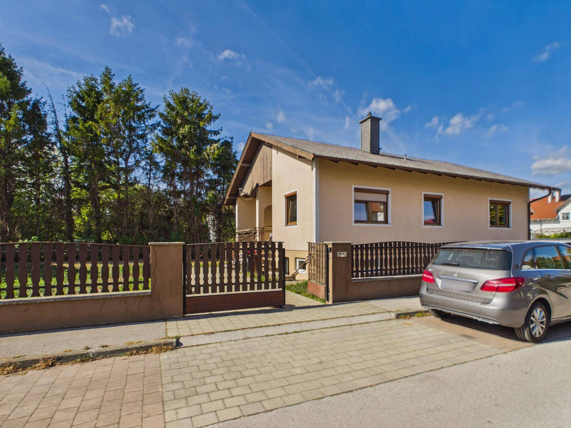 Ansicht des Hauses von der Straße mit Zaun, gepflasterter Zufahrt und Parkplatz.