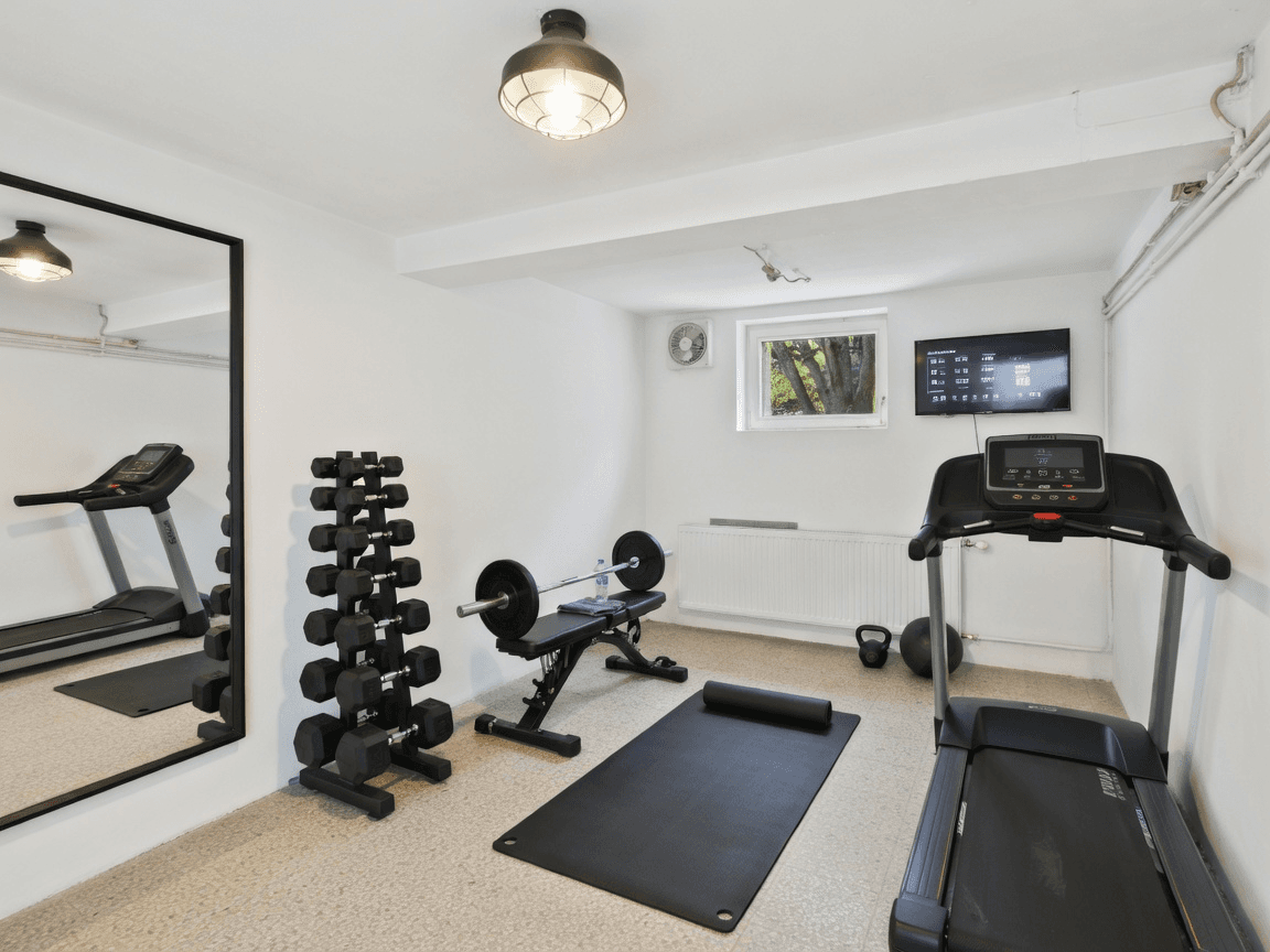 Fitnessraum im Keller mit Laufband, Hanteln und Fenster für Tageslicht.
