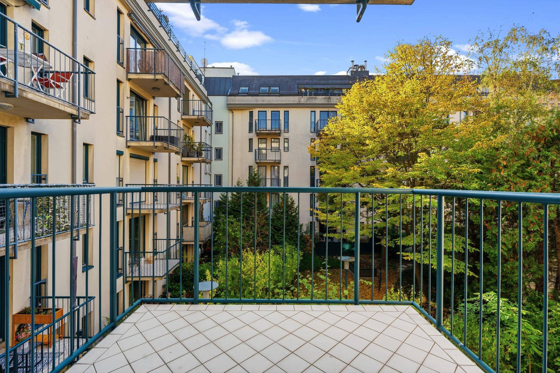 Balkon mit Fliesenboden und Blick auf den begrünten Innenhof des Wohnkomplexes.