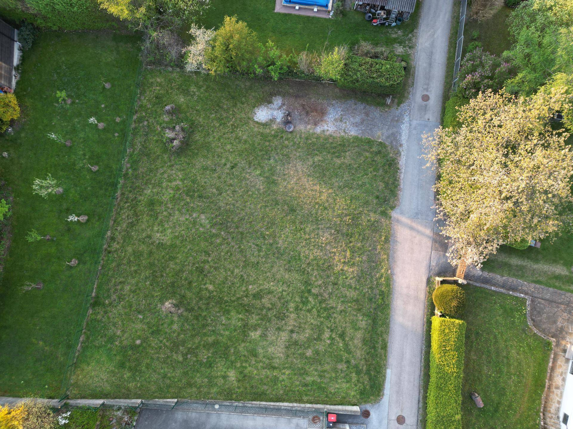 Draufsicht auf ein grünes Grundstück mit Rasenfläche und angrenzender Straße in einer Wohngegend.