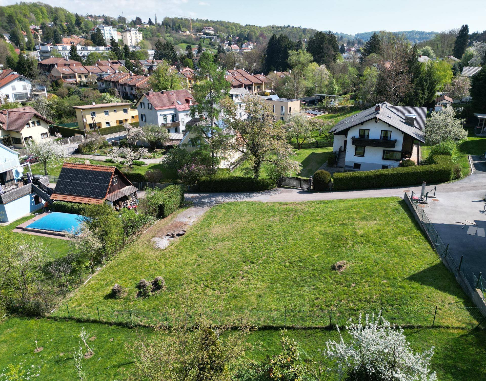 Weitläufiges grünes Grundstück in einer Wohnsiedlung mit angrenzenden Häusern und einem Poolbereich.