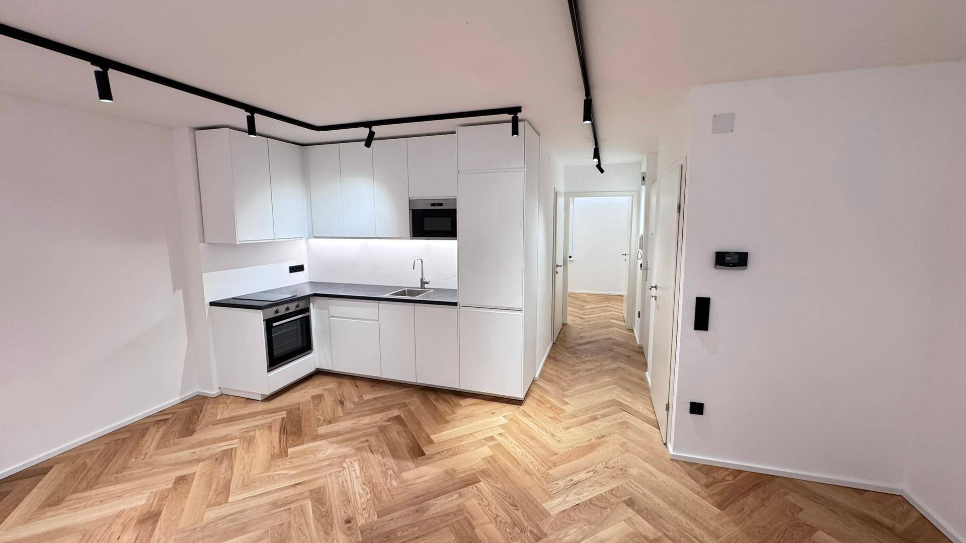 Moderne Einbauküche mit weißen Schränken, dunkler Arbeitsplatte und Fischgrätparkettboden.