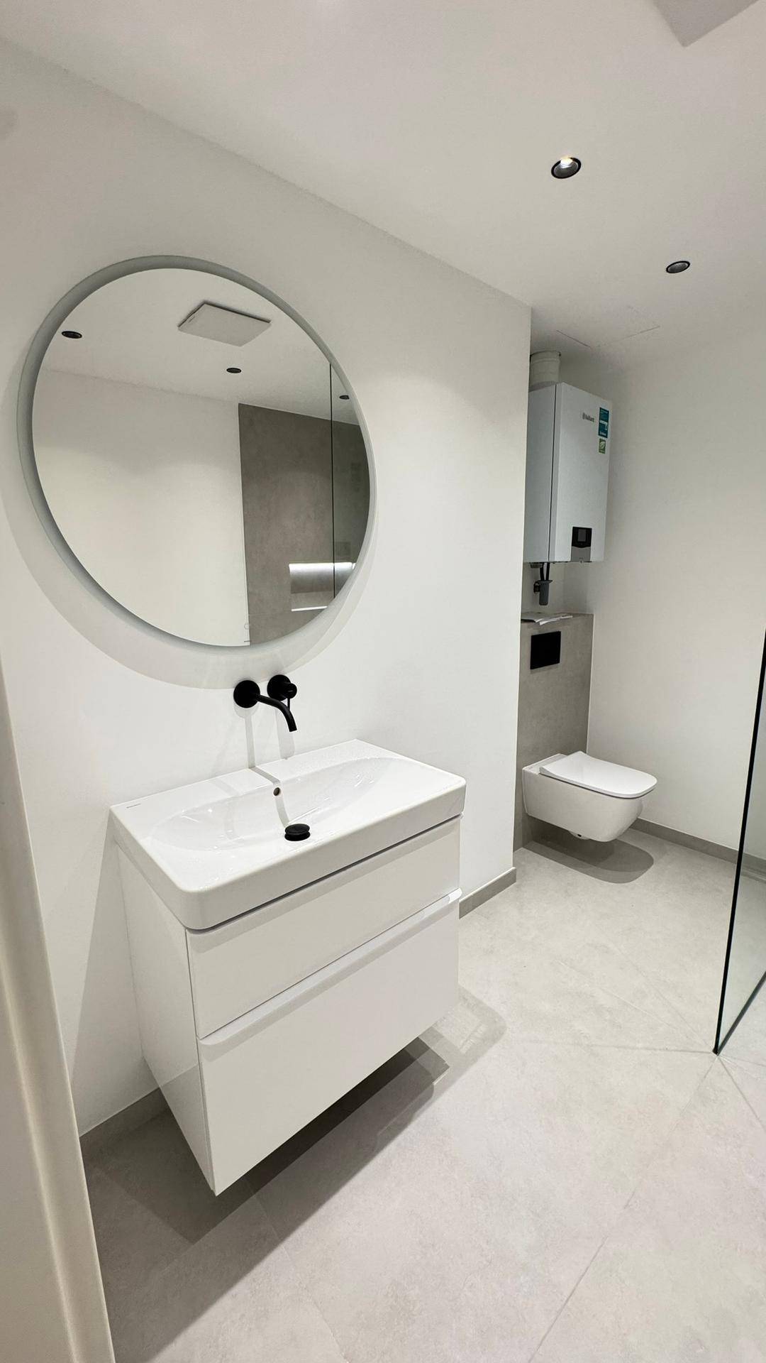 Detailansicht des modernen Badezimmers mit Waschtisch, rundem Spiegel und Hänge-WC.