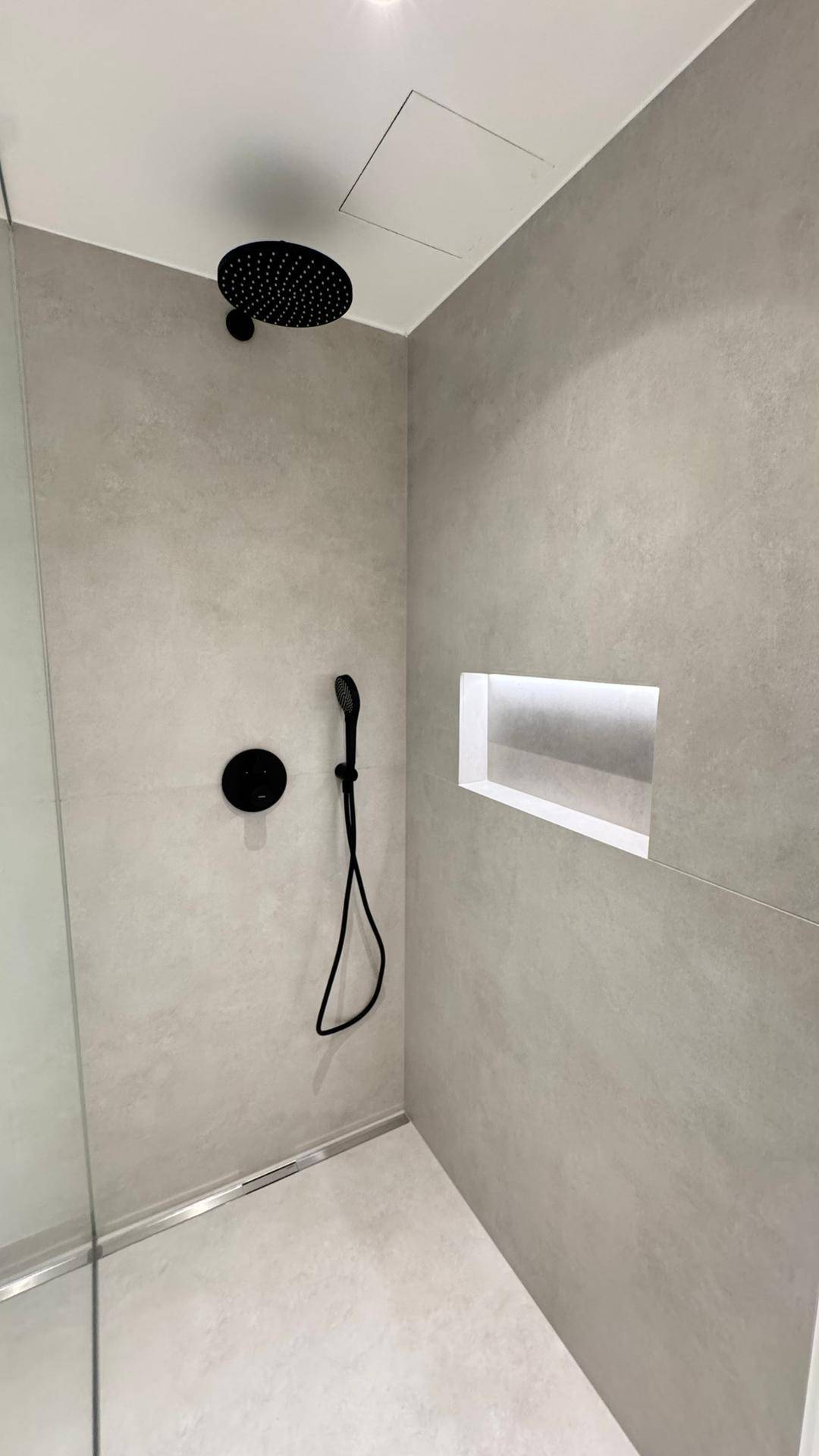 Nahaufnahme der modernen Regendusche mit schwarzem Duschkopf und praktischer Ablagenische.