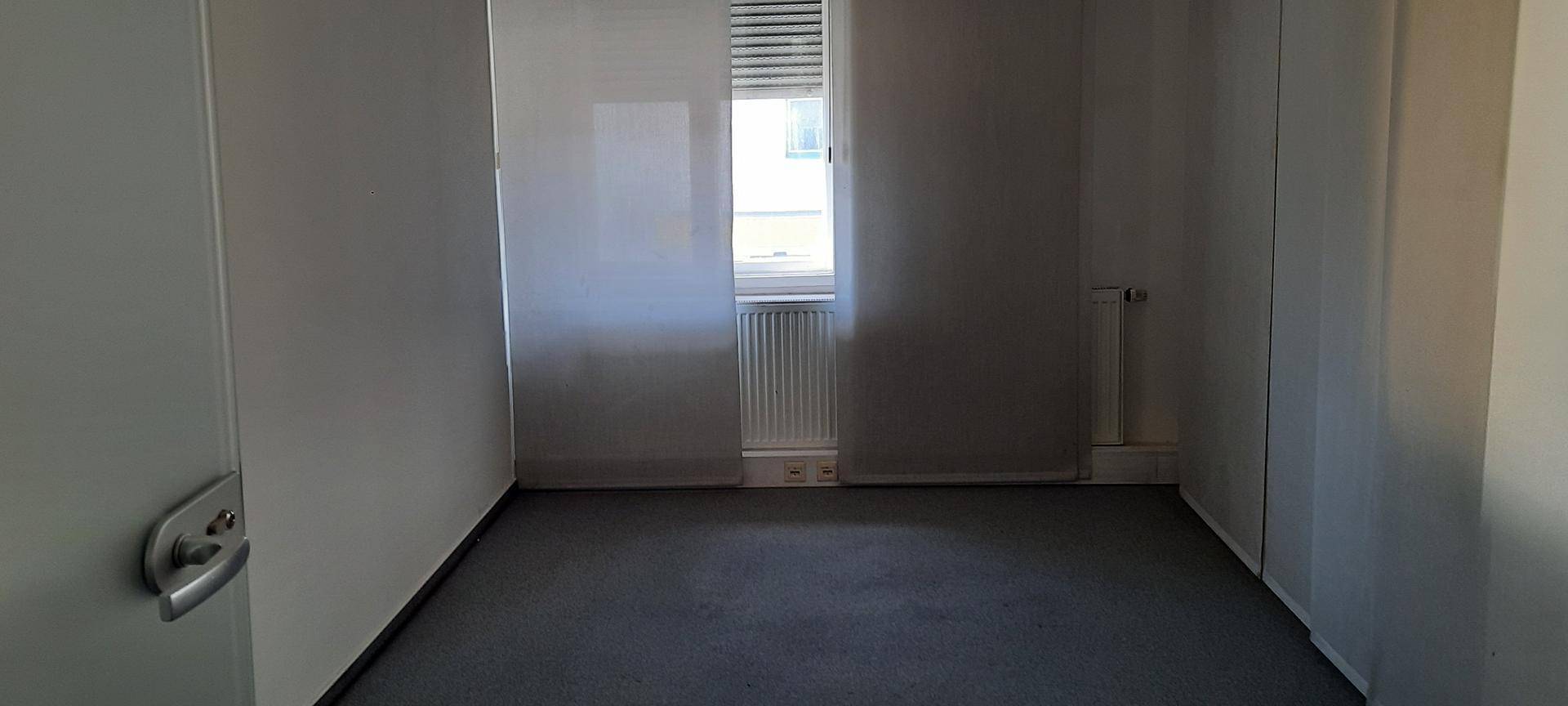 Kleiner Büroraum mit Fenster, Jalousien und grauem Teppichboden, ideal für Einzelbüros.