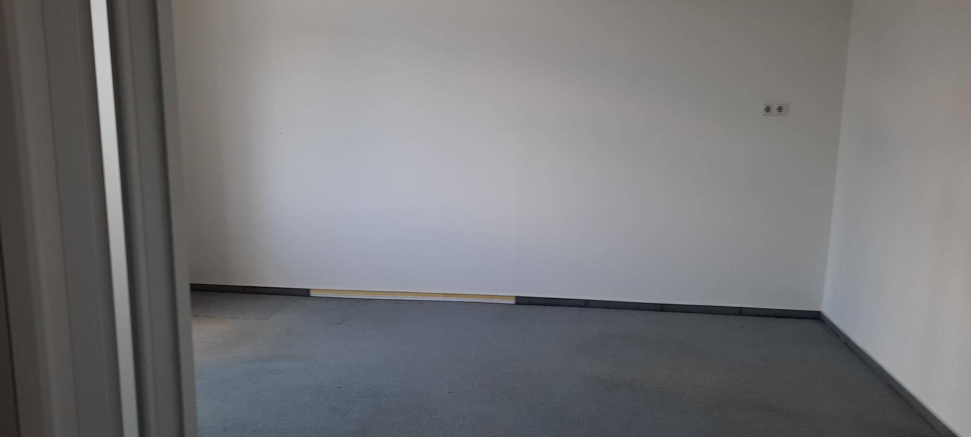 Leerer, sauberer Büroraum mit grauem Teppichboden und weißen Wänden, bereit zur sofortigen Nutzung.