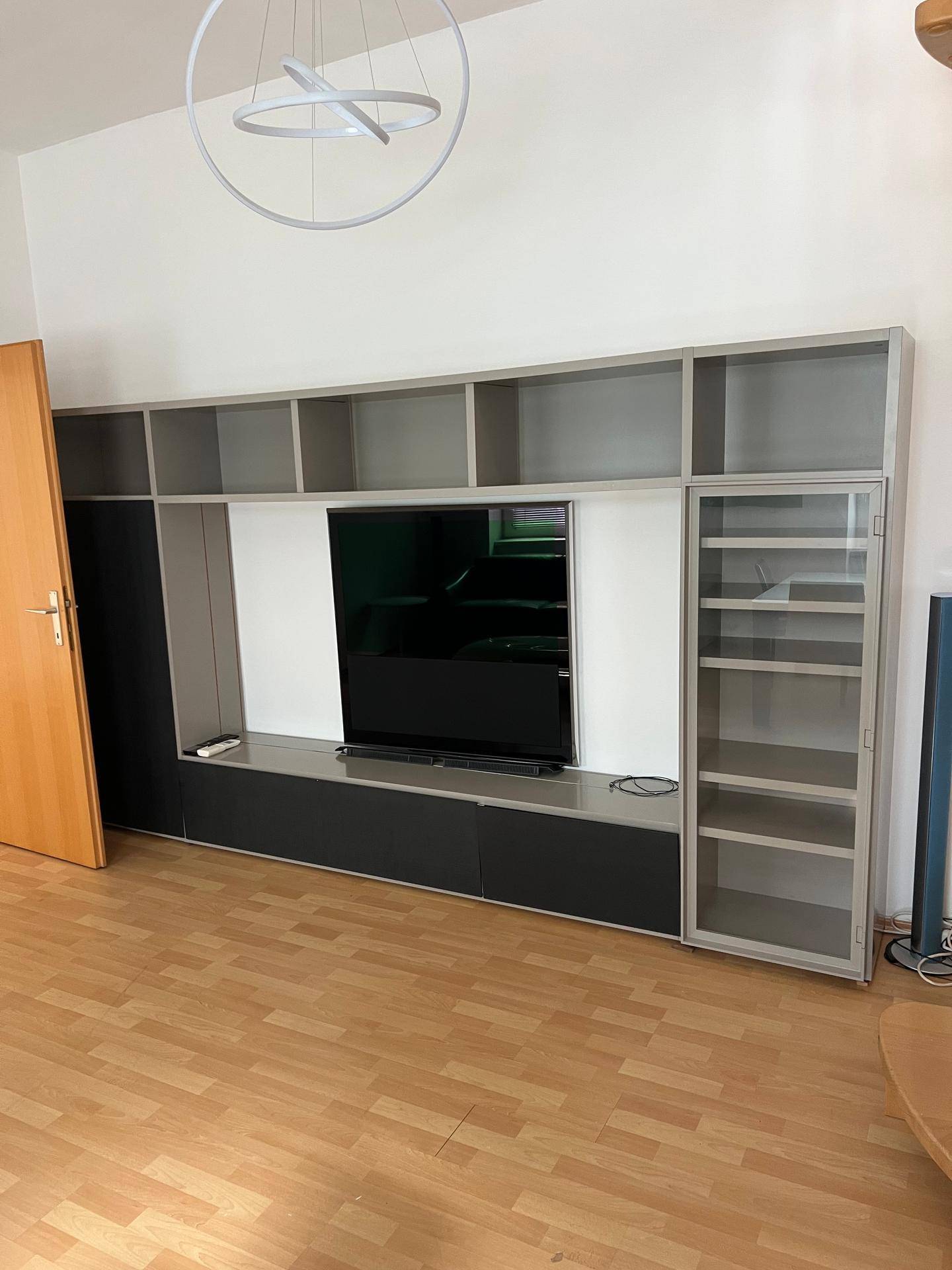 Wohnzimmer mit großer grauer Medieneinheit und Fernseher, auf Laminatboden stehend.