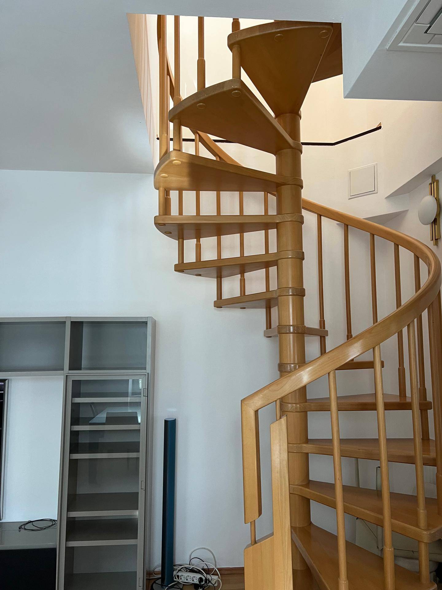 Elegante Holzwendeltreppe in einem hellen Raum mit weißen Wänden und Laminatboden.
