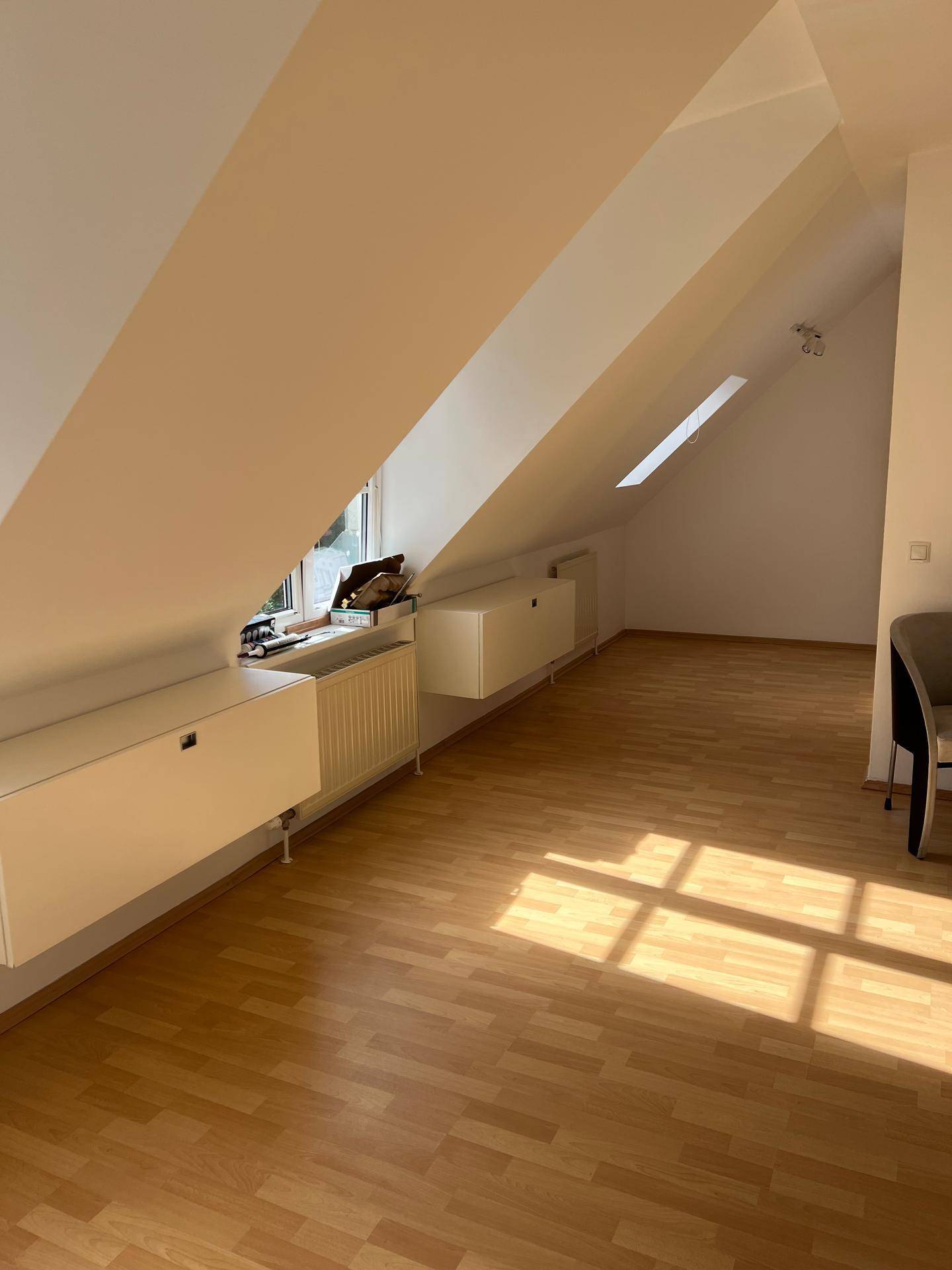 Sonniges Dachzimmer mit schrägen Decken, Fenster und Laminatboden, mit integrierten Schränken.