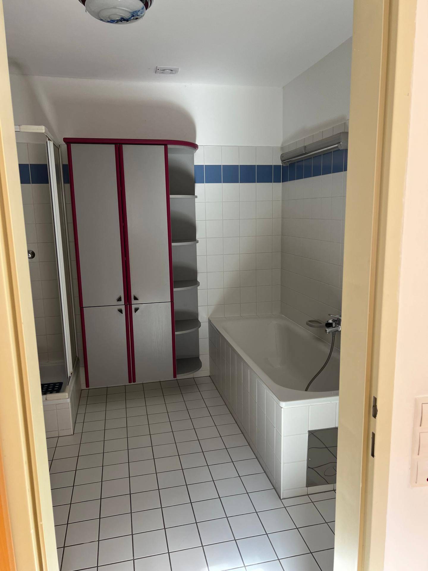 Badezimmer mit Badewanne, Duschkabine und farbigen Einbauschränken, komplett gefliest.