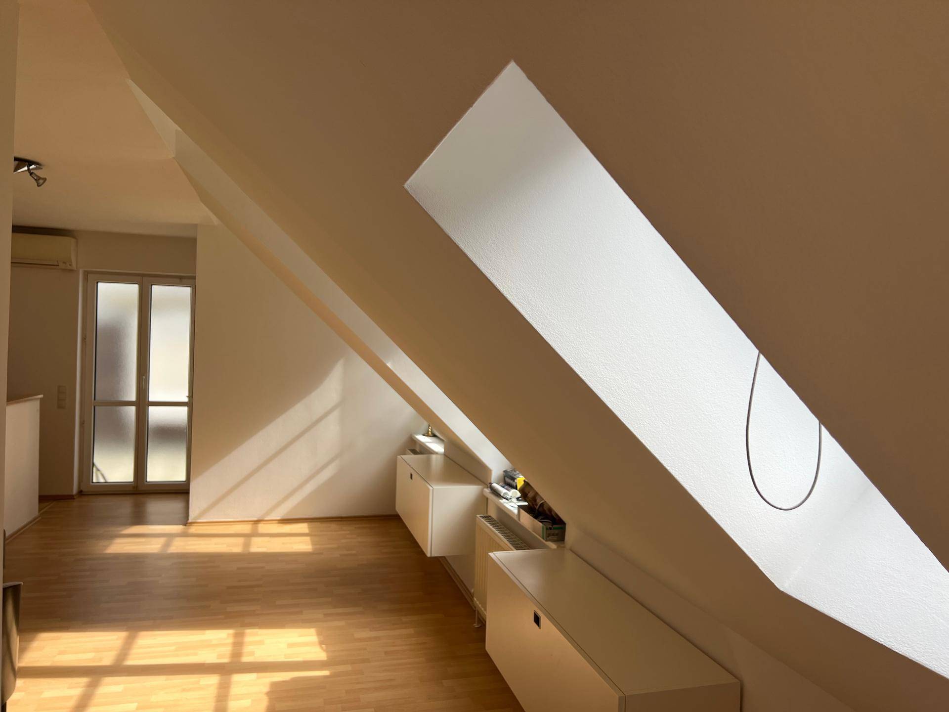 Heller Dachraum mit schrägen Decken, Dachfenster und Laminatboden, ausgestattet mit Einbauschränken.