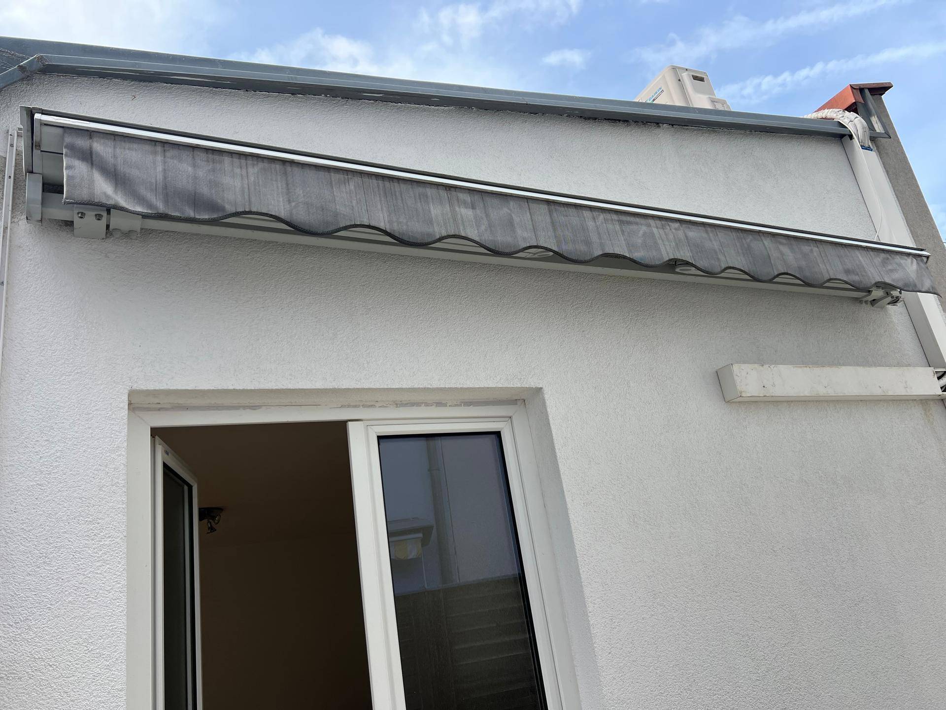 Weiße Fassade des Gebäudes mit einem Fenster und einer ausgefahrenen grauen Markise.