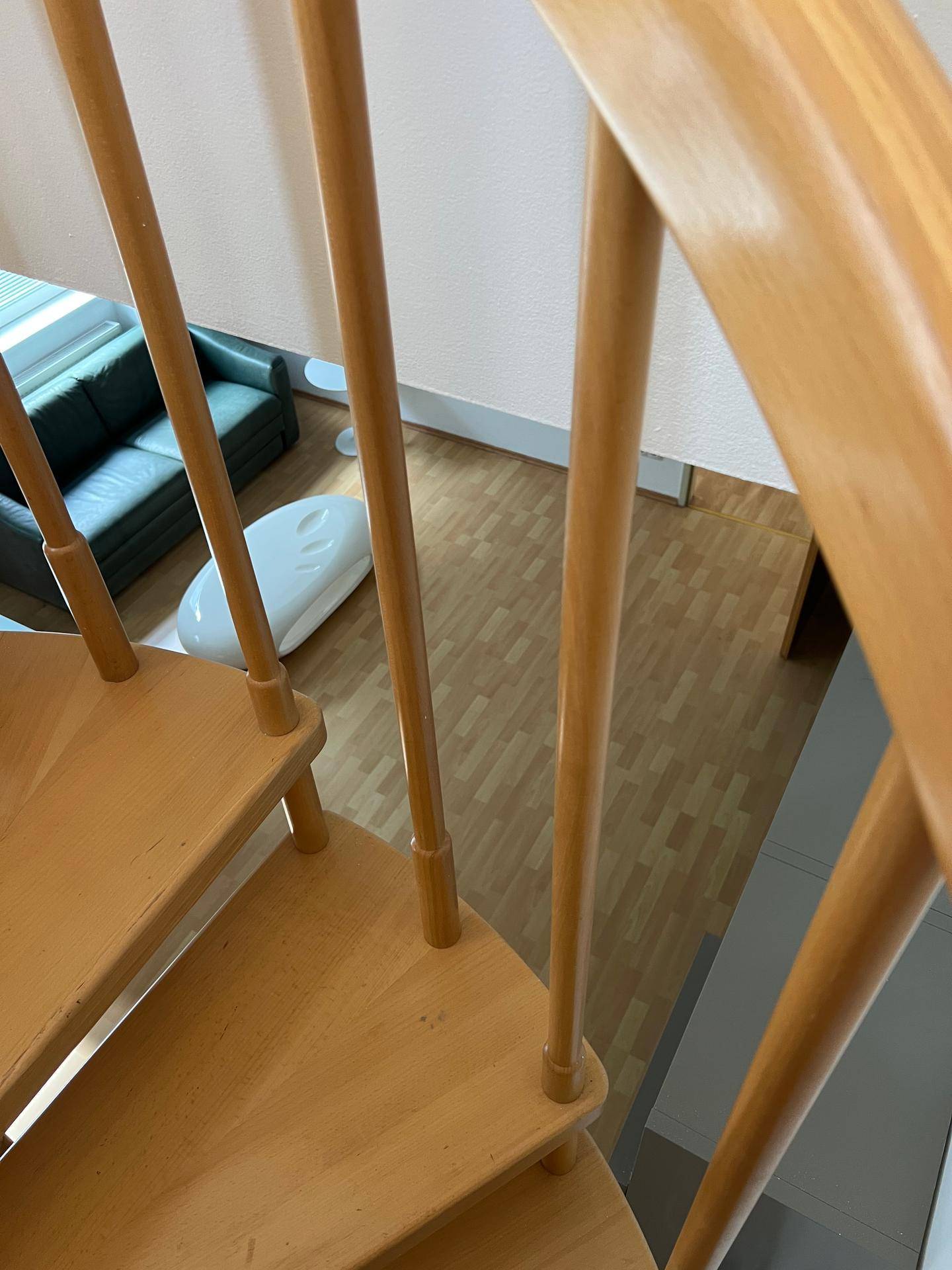 Detailansicht einer Holzwendeltreppe, die zu einem Wohnbereich mit Laminatboden führt.