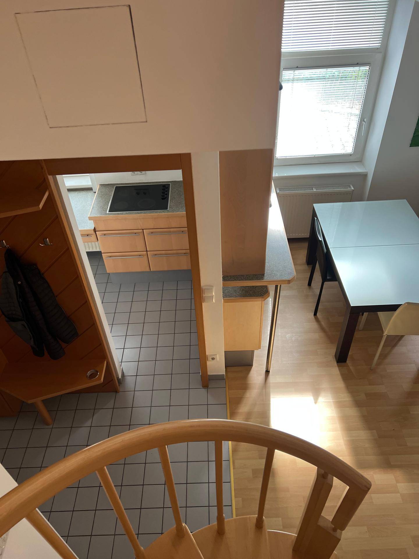 Blick von der Holzwendeltreppe auf einen offenen Wohn-Essbereich mit angrenzender Küche.
