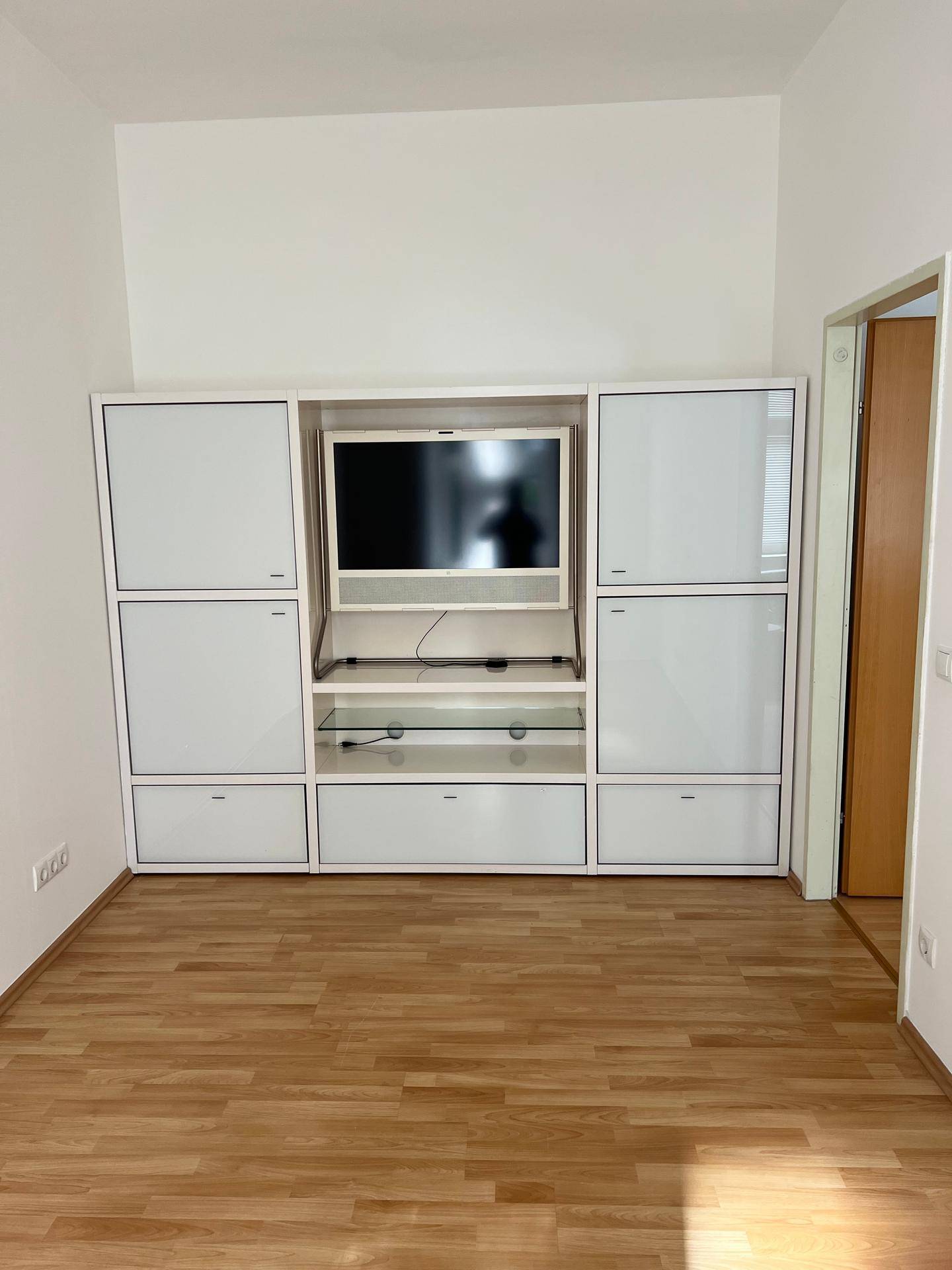 Wohnzimmer mit weißer Medieneinheit und Fernseher, ergänzt durch Laminatboden.