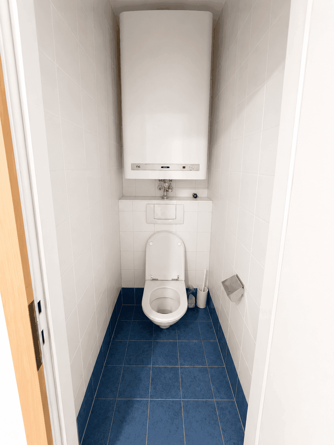 Kleines WC mit blauen Bodenfliesen, weißen Wandfliesen und einem Wand-WC.