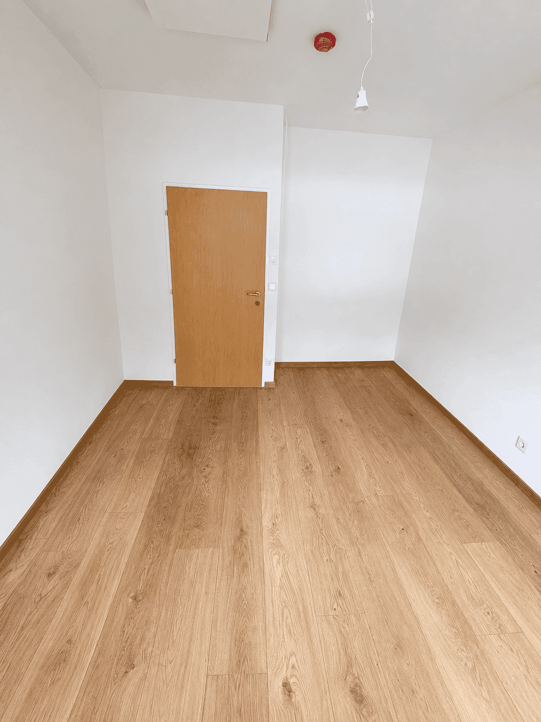 Schlichtes, leeres Zimmer mit Holzplankenboden und einer einfachen Holztür.