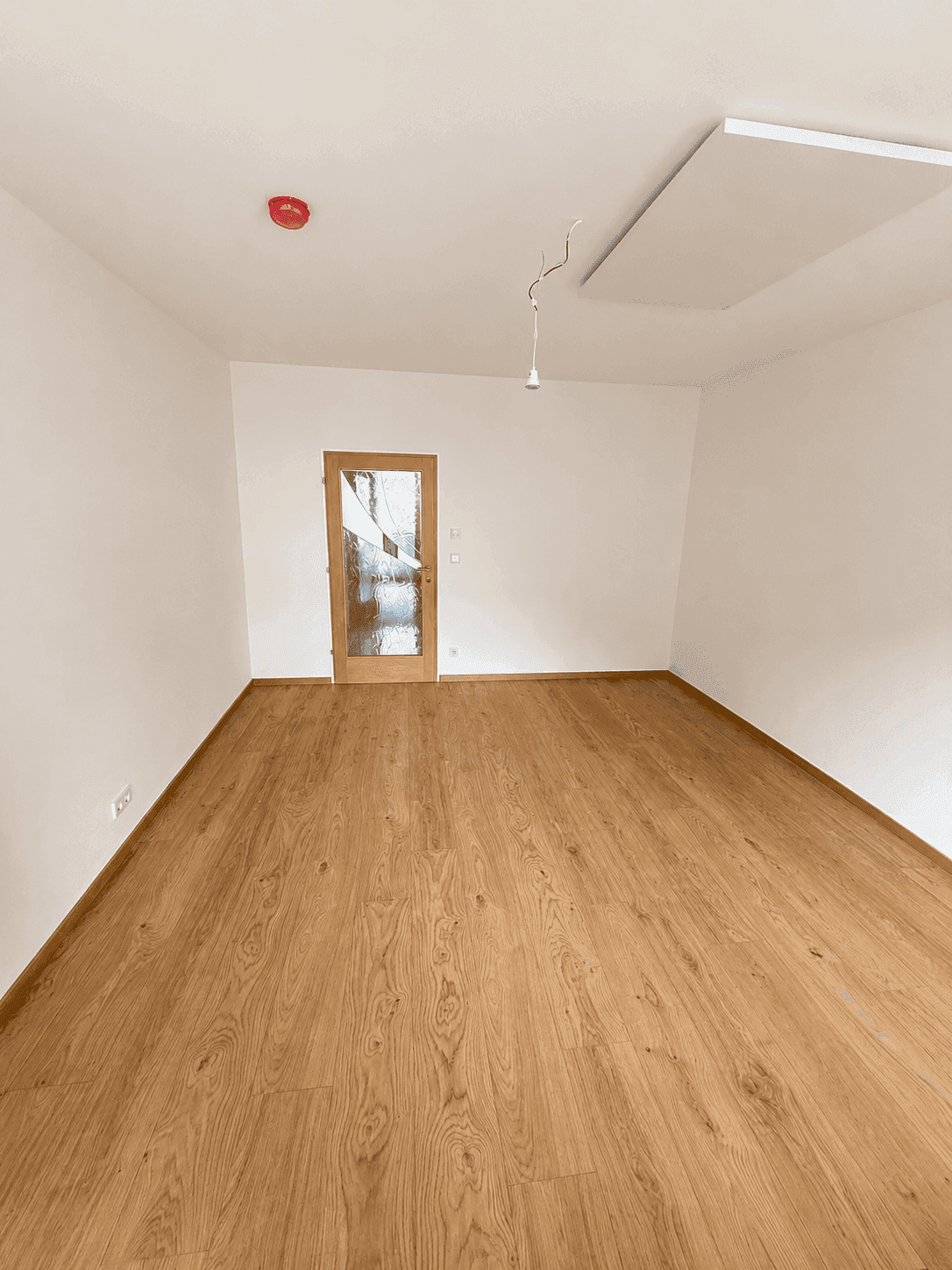Leeres Zimmer mit warmem Holzplankenboden und einer Holztür mit Milchglas.