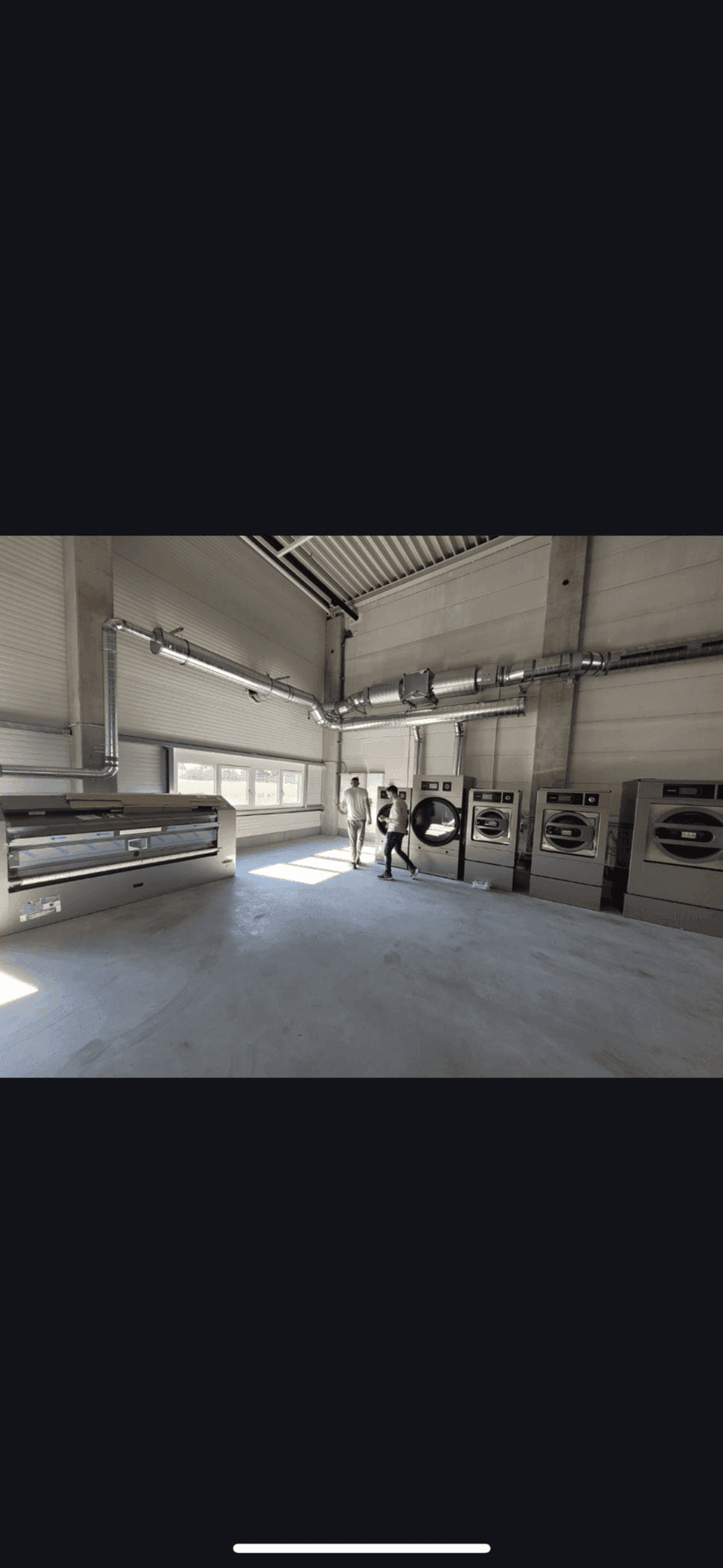 Geräumiger Industrieraum mit professionellen Waschmaschinen und Bügelgeräten, gut beleuchtet durch große Fenster.