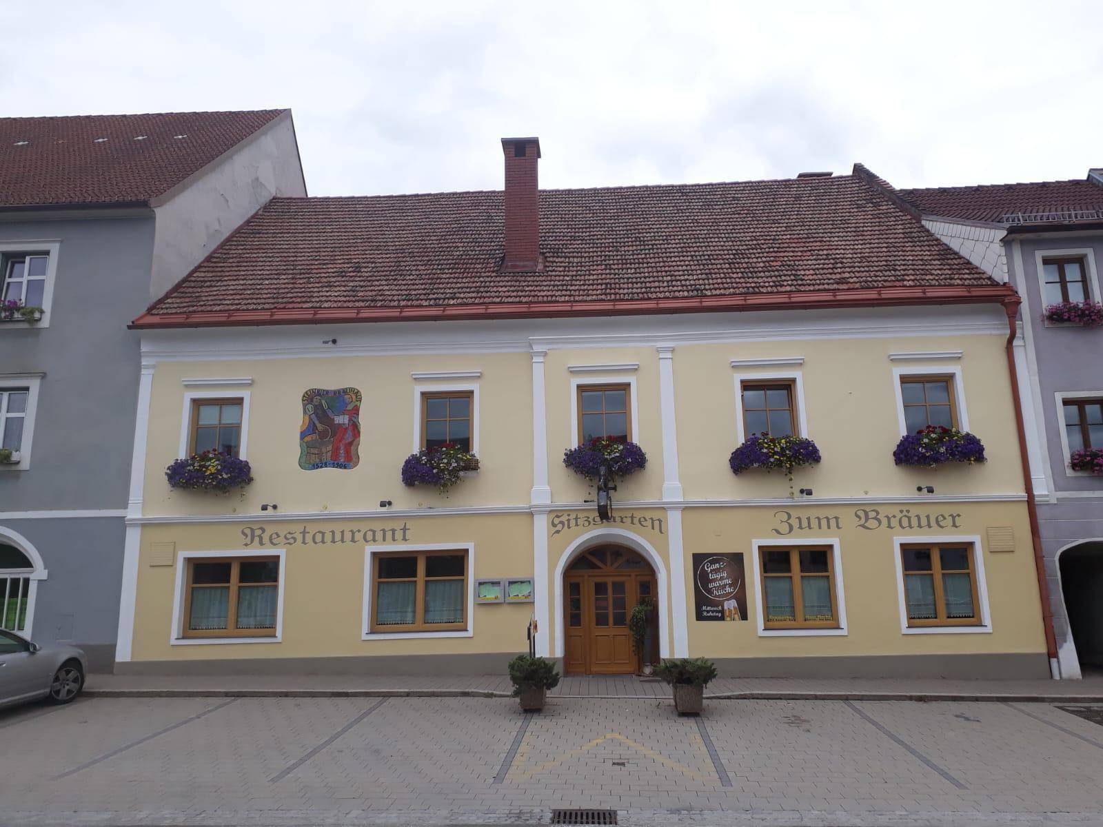 Traditionelles Gebäude mit Restaurantfassade, Blumenkästen und Sitzgarten-Eingang unter bewölktem Himmel.