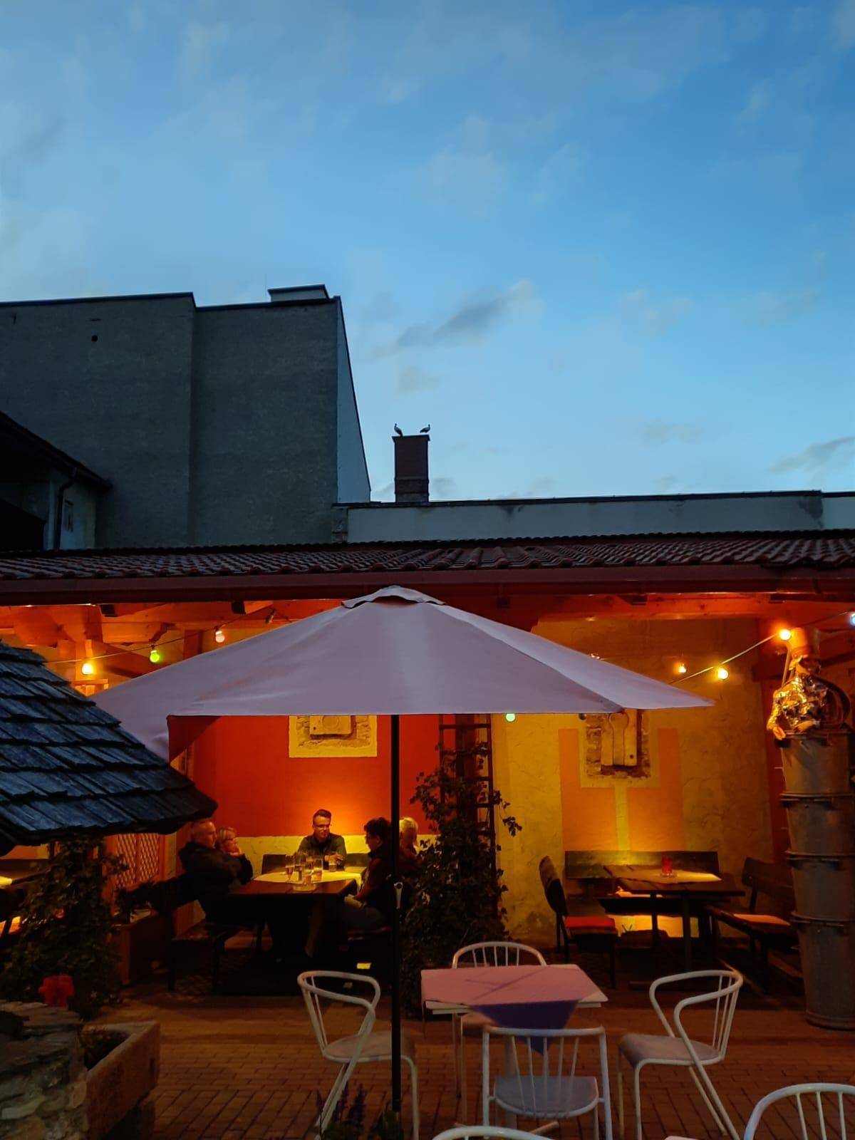 Gemütlicher Außenbereich mit Tischen, Stühlen und Lichterketten bei Dämmerung unter blauem Himmel.