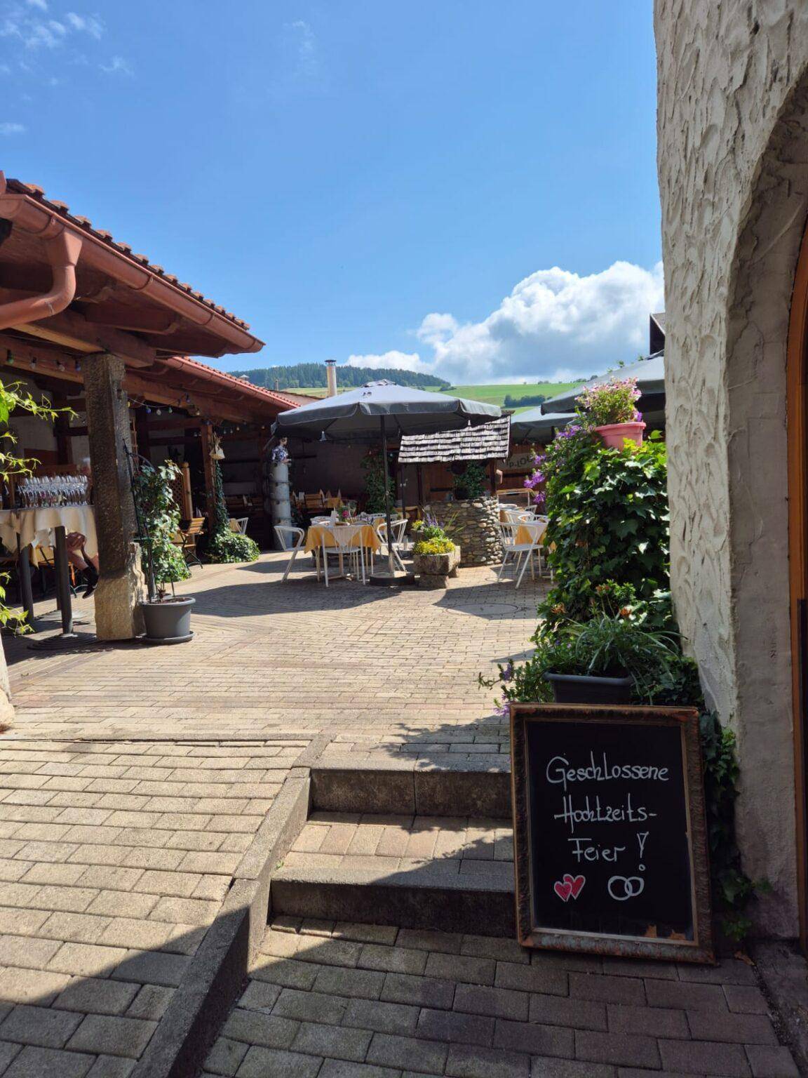 Sonniger Innenhof mit gepflastertem Boden, Stufen und weiteren Sitzgelegenheiten im Freien mit grüner Aussicht.