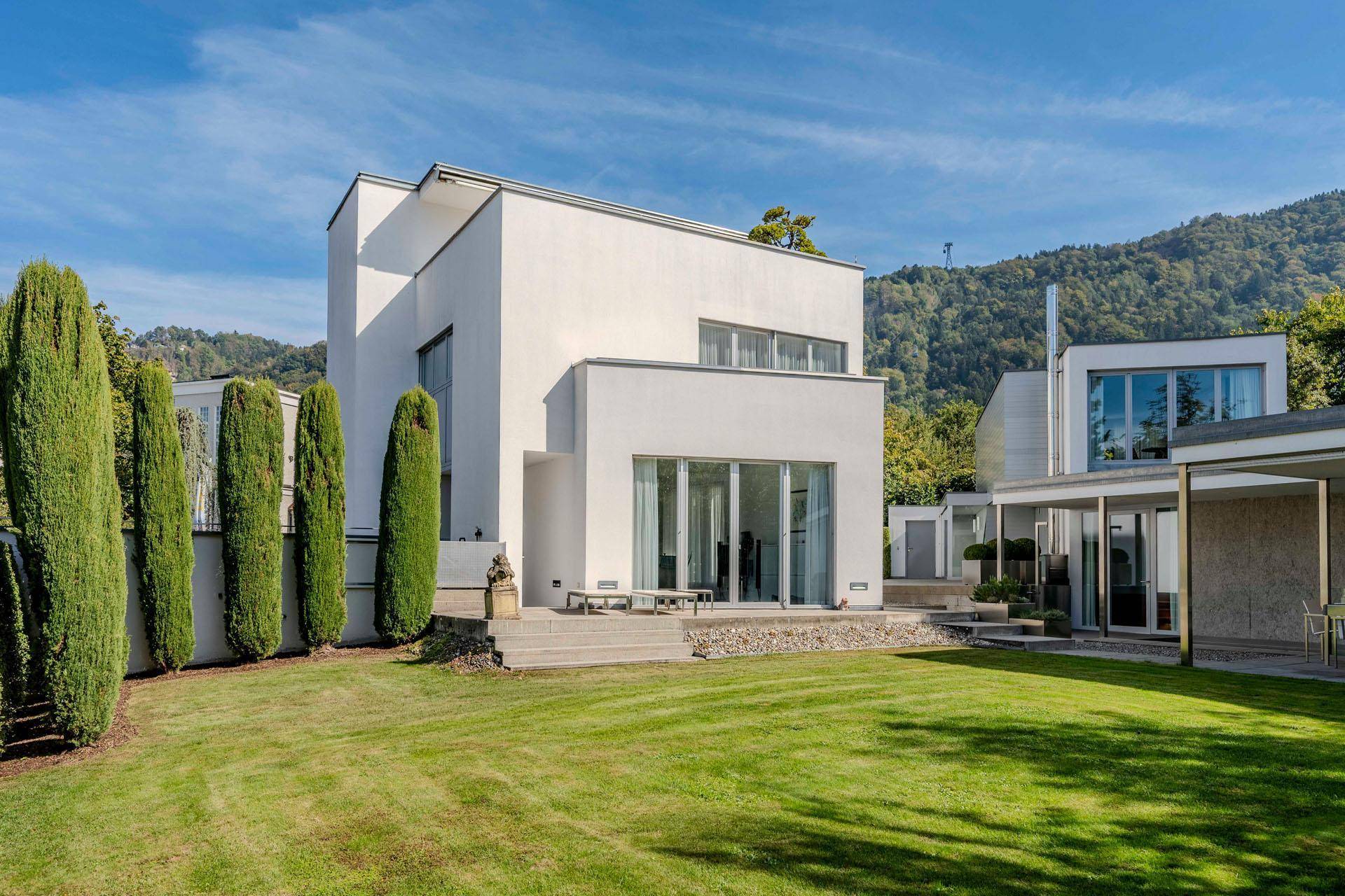 Elegante moderne Villa mit gepflegtem Garten und Blick auf die bewaldeten Hügel.
