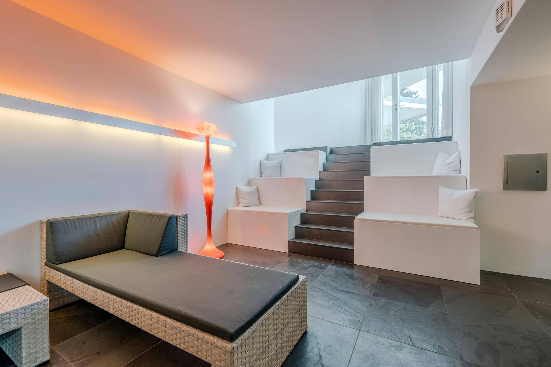 Entspannungsbereich mit Liege und gestuften Sitzgelegenheiten, beleuchtet von einer modernen Stehlampe.