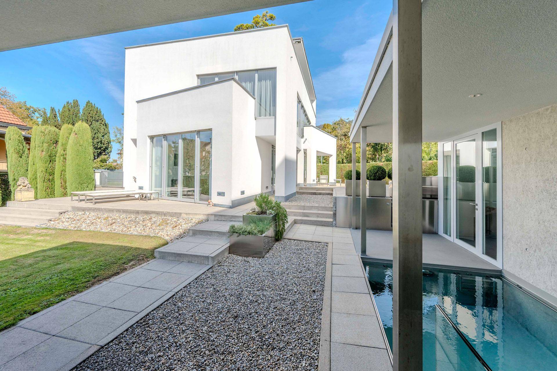 Moderner Gartenbereich mit Wasserbecken, Kiesweg und Blick auf die Villa.