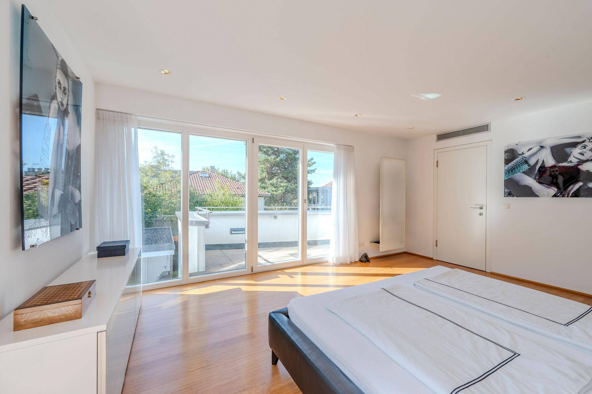 Helles Schlafzimmer mit Holzboden, großen Fenstern und Zugang zur Dachterrasse.