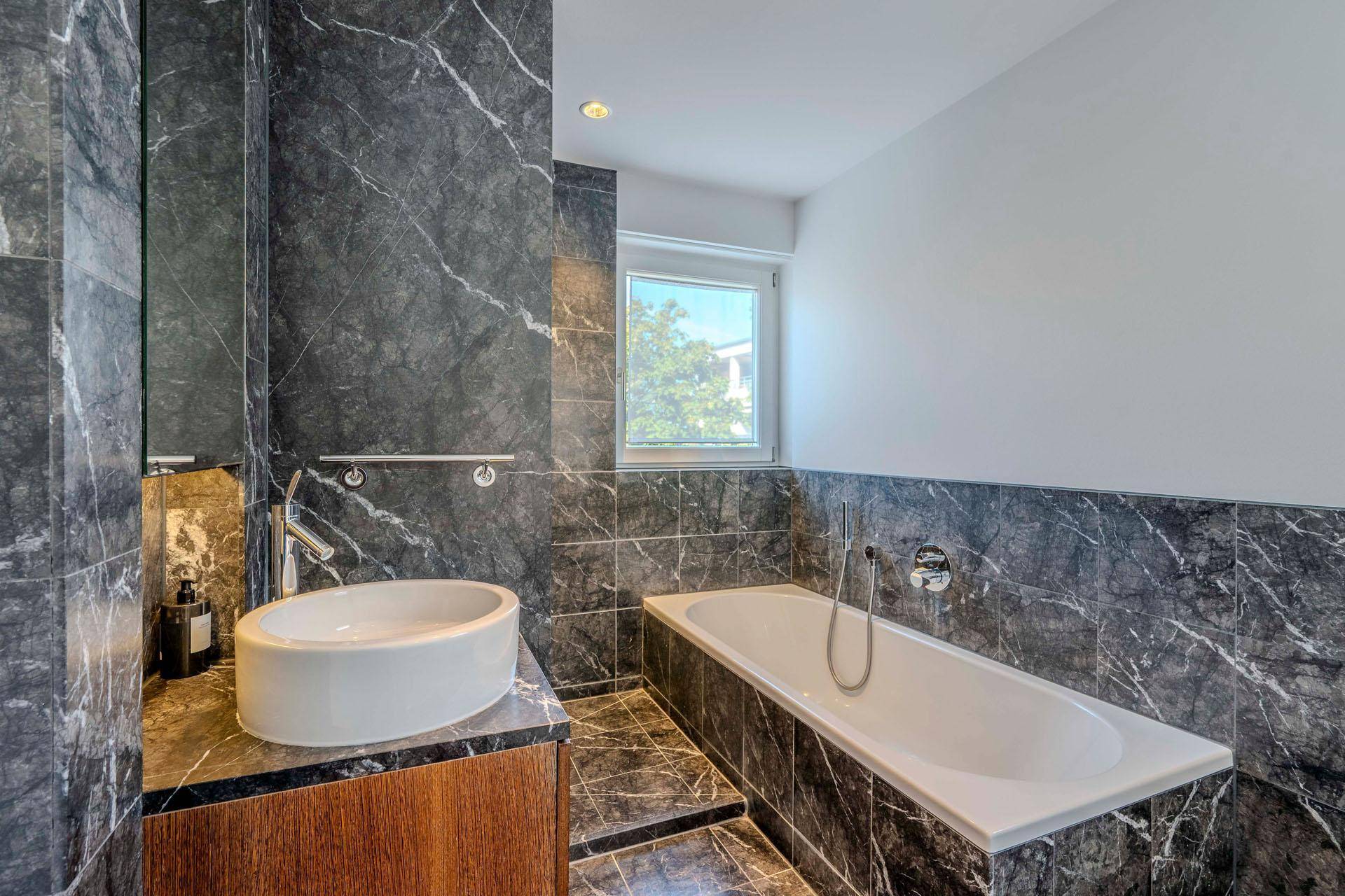 Elegantes Badezimmer mit dunklen Marmorfliesen, ovalem Waschbecken und Badewanne.